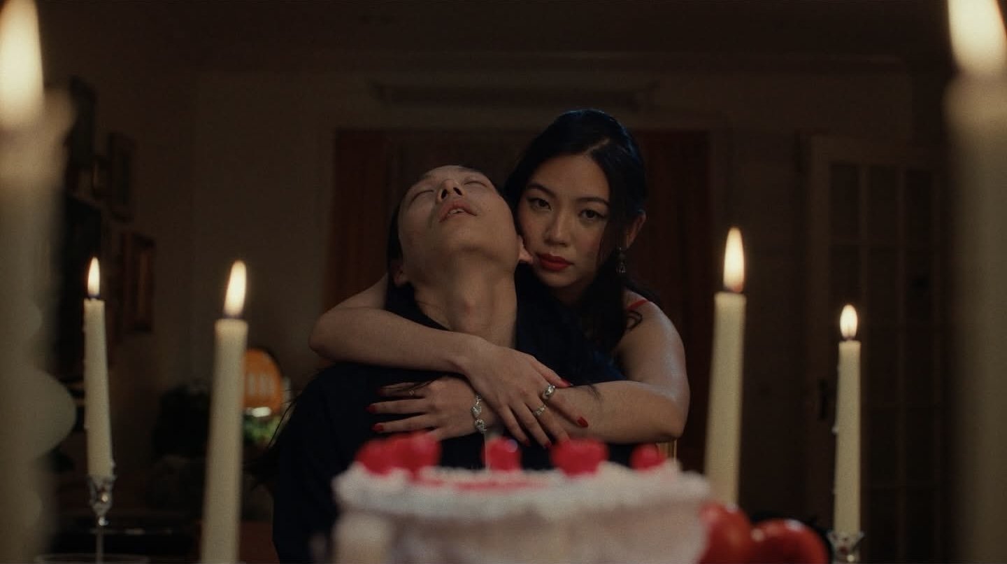 A young woman hugging an older woman in a dimly lit room, with a cake and candles in the foreground.
