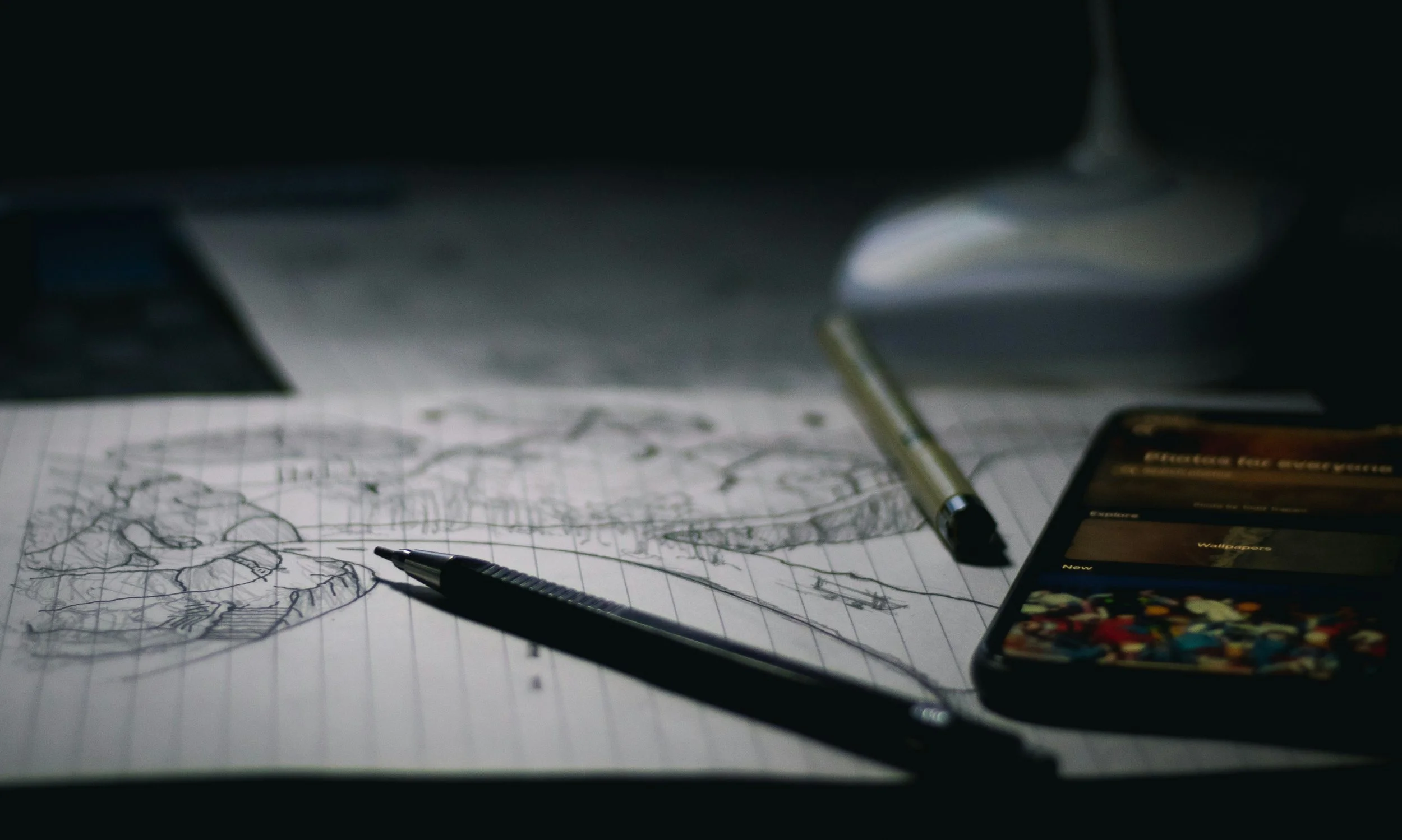 Sketch of a landscape on graph paper with a pen, a tablet displaying a menu, and a stylus on a dark background.
