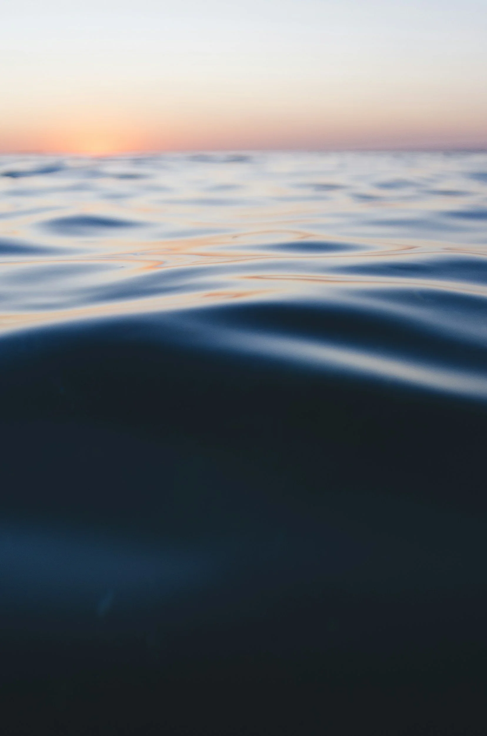 Close-up view of calm ocean water at sunset with soft sunlight reflecting on gentle waves.