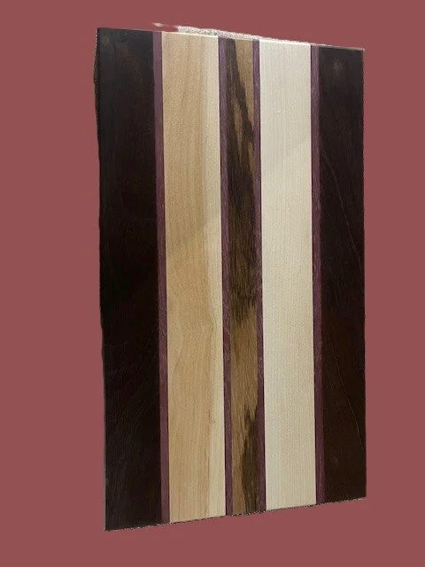 A wooden wall art piece with vertical striped panels in shades of dark brown, light beige, and cream, set against a muted pink background.