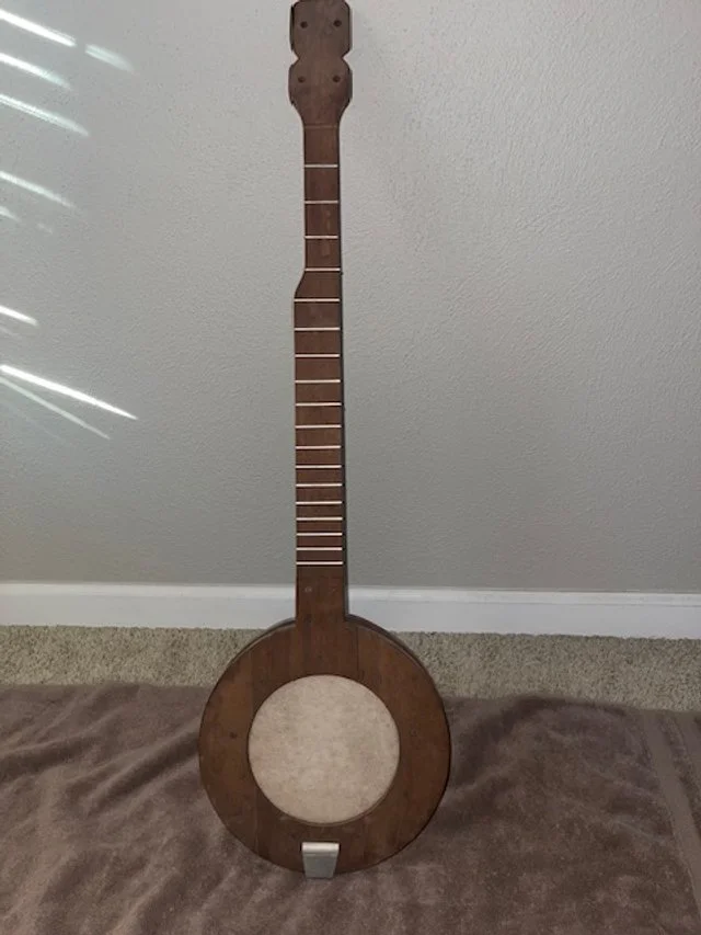 Wooden guitar-shaped wall decor with no strings and no strings or sound hole, leaning against a wall and resting on a brown carpet.