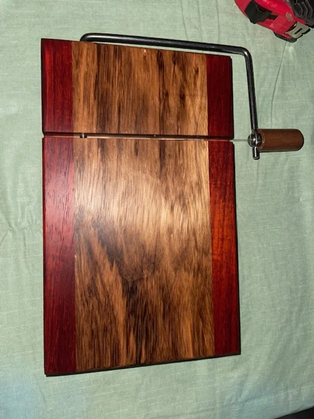 A wooden board with a clamp attached to the top right corner, resting on a green fabric surface, with a red tool in the background.