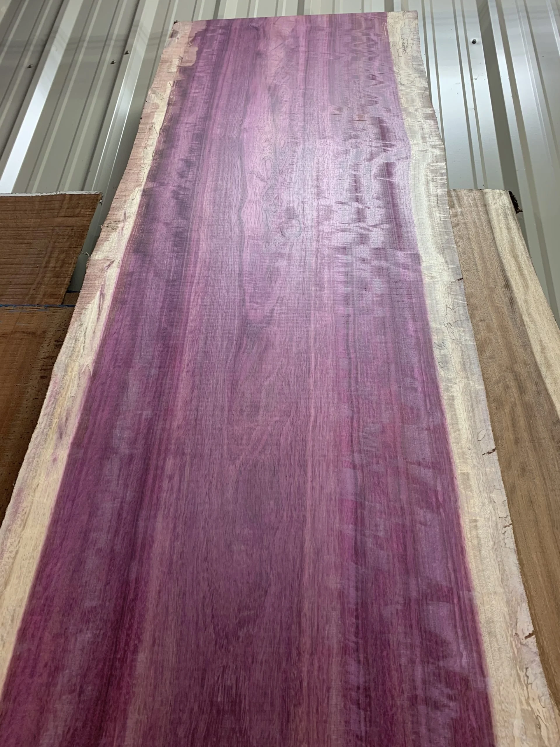 A large, unfinished piece of wood with a pink and purple finish laid on a metal surface.