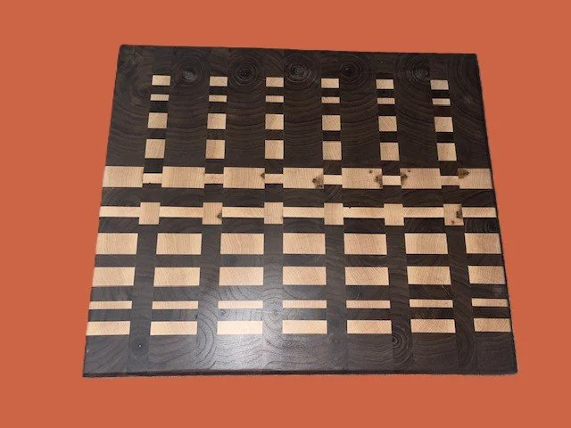 A wooden chessboard with alternating light and dark squares, positioned on a reddish surface.