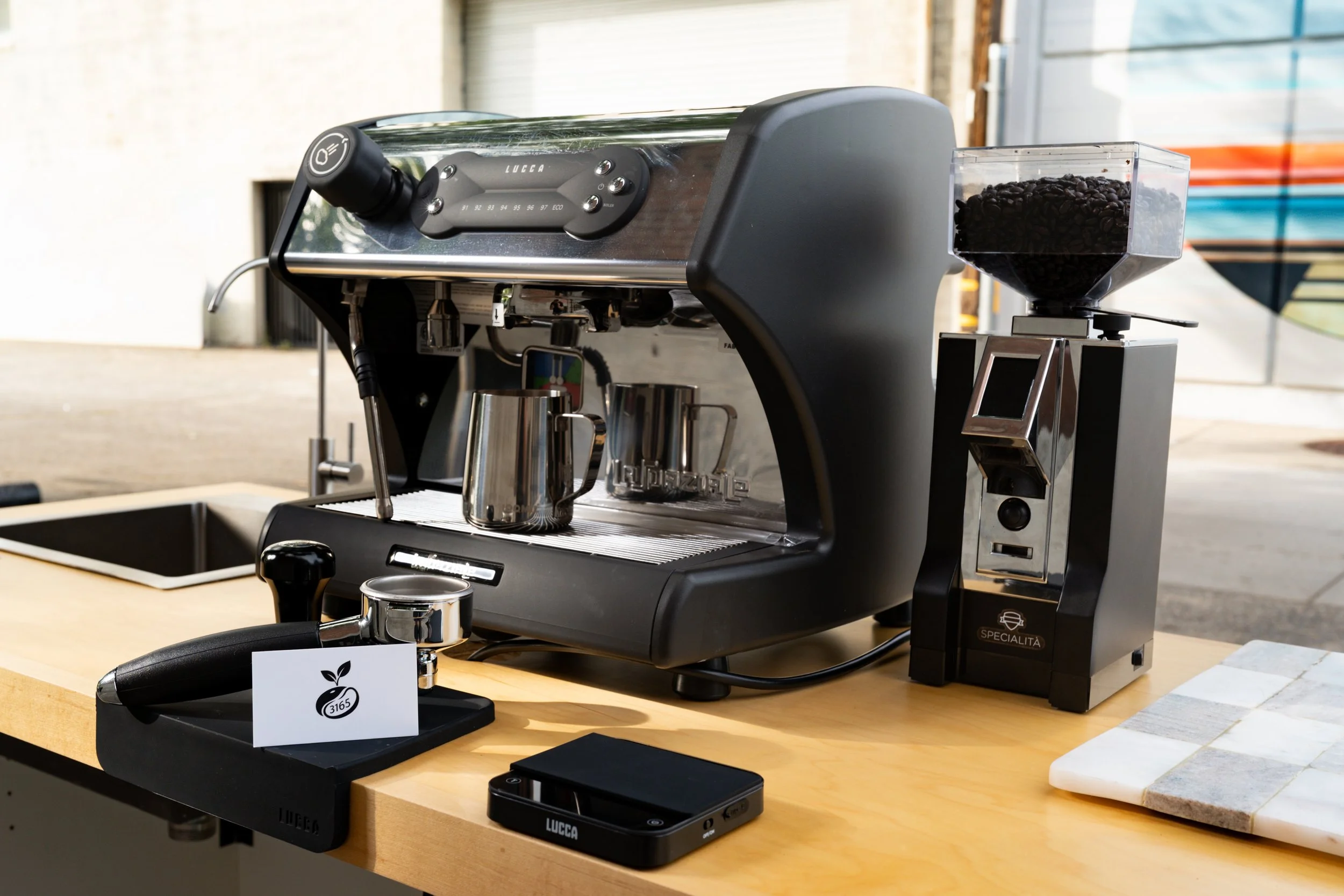 A professional espresso machine with a portafilter, coffee grinder, and freshly roasted coffee beans displayed on a wooden countertop at the 3165 Coffee mobile espresso bar in Sacramento, California.