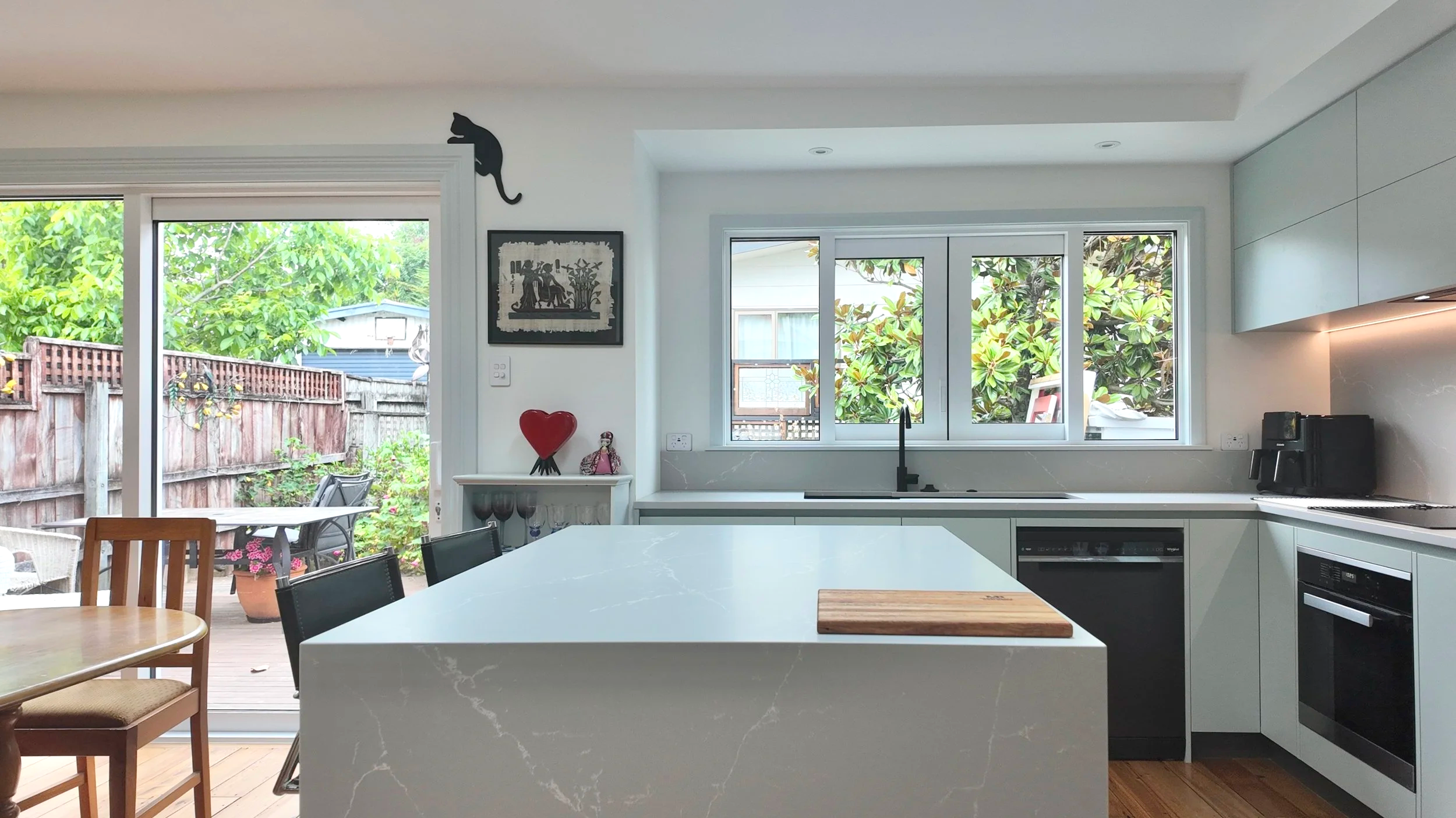 Modern kitchen with white cabinetry, a central island, a view of a backyard through sliding glass doors, and countertop appliances.