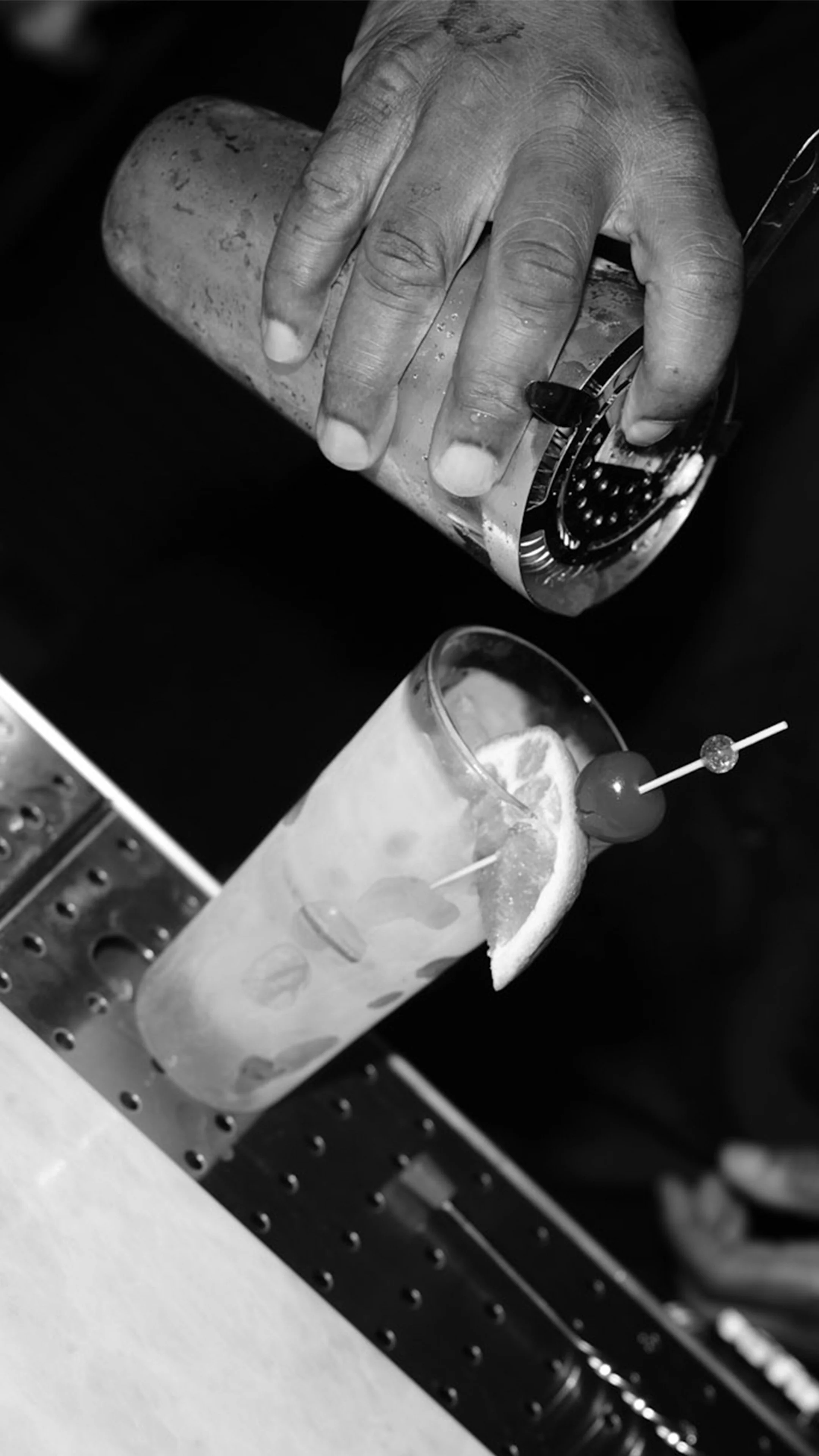 A bartender pouring a craft cocktail through a strainer into an iced glass garnished with a citrus wedge and cherry at Roosevelts Restaurant & Bar at Live Oaks Golf Club in Jackson, Mississippi.