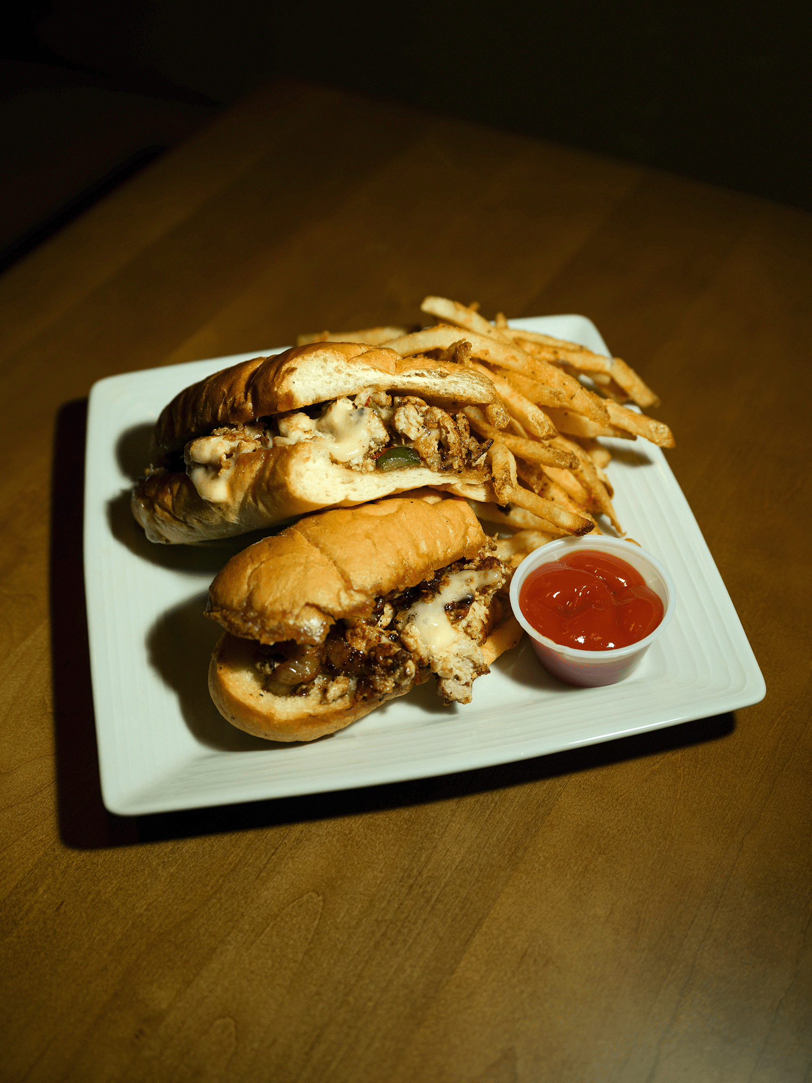 A chicken cheesesteak sandwich served at Roosevelts Restaurant & Bar at Live Oaks Golf Club in Brandon, Mississippi. Loaded with grilled chicken, peppers, onions, and melted cheese on a hoagie roll, served with seasoned fries and ketchup.