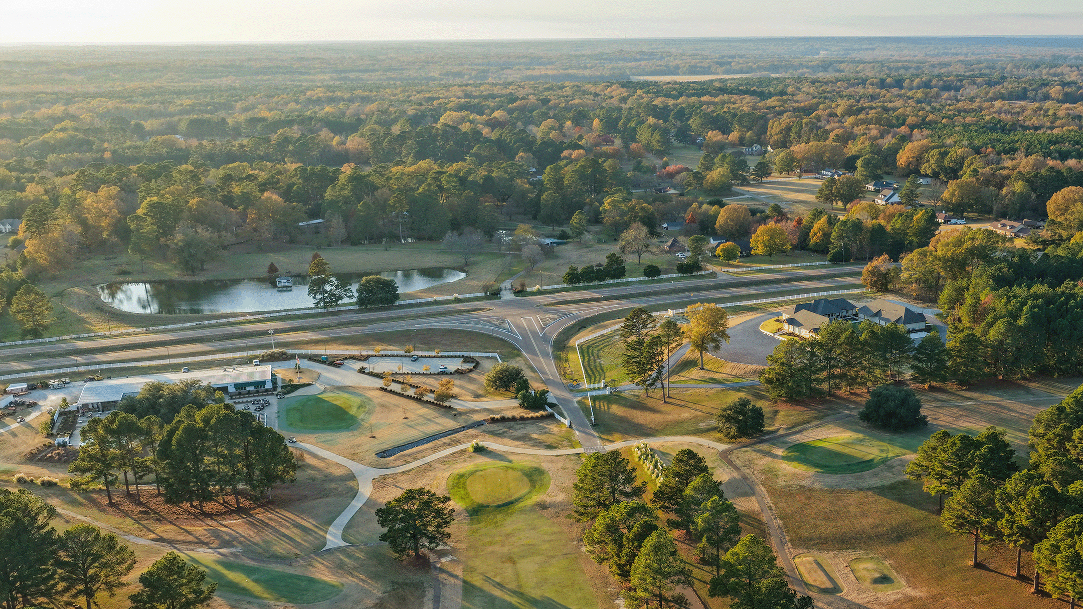 Aerial view of a suburban park with golf courses, a pond, residential homes, roads, and lush green trees during daytime.