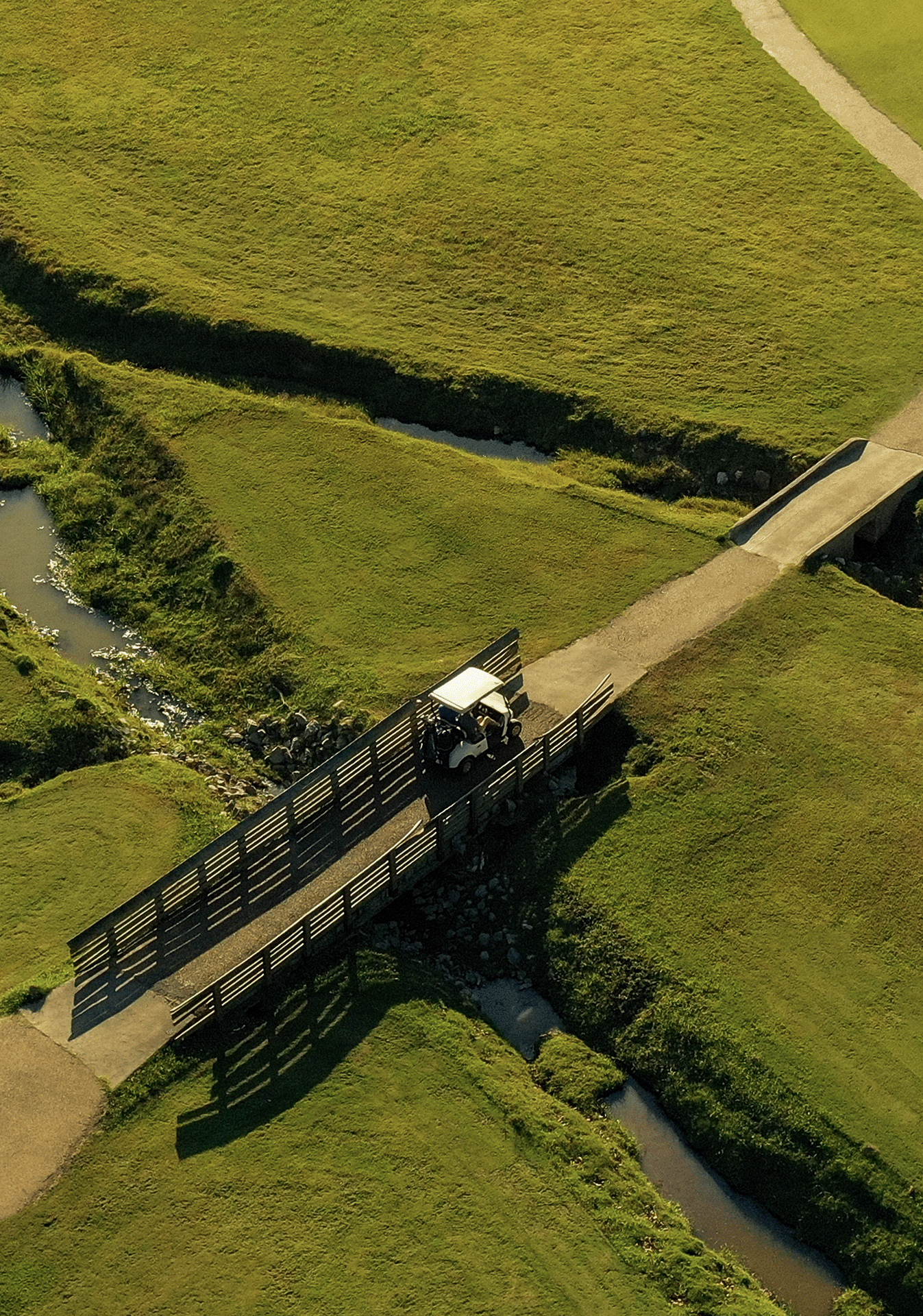 A small golf cart parked on a wooden bridge over a small creek in a grassy area.