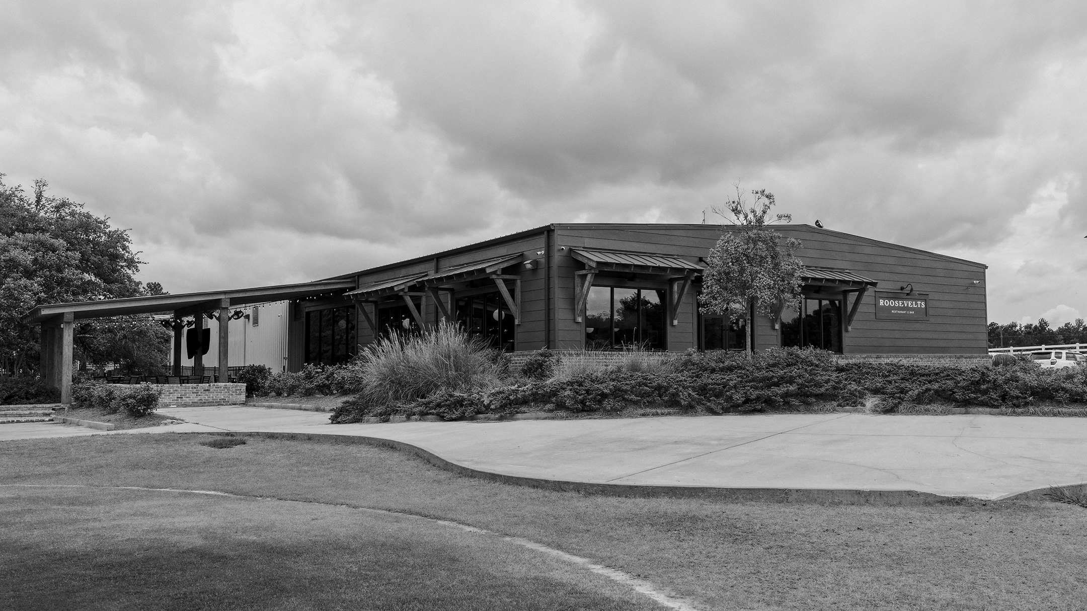 Exterior view of Roosevelts Restaurant & Bar at Live Oaks Golf Club in Jackson, Mississippi, featuring modern farmhouse-style architecture with covered walkway and outdoor seating