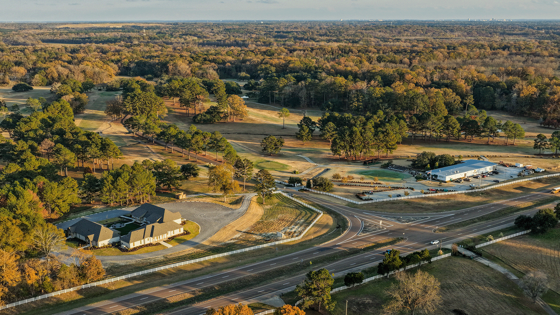 Aerial view of Live Oaks Golf Club in Jackson, Mississippi, showing the golf course, clubhouse, tree-lined fairways, white fencing, and surrounding landscape along the highway at golden hour.