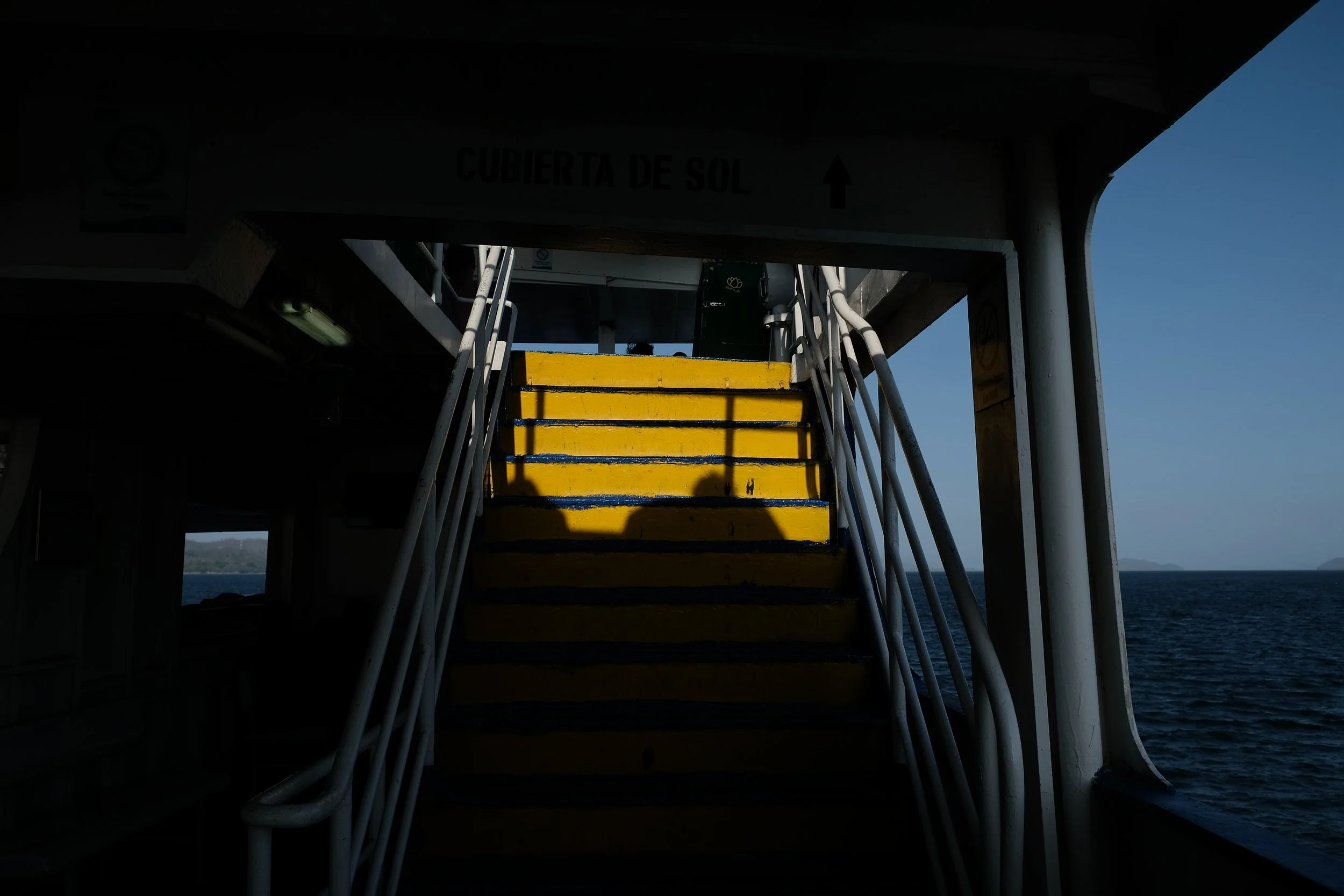 Yellow stairs on a boat with the sea in the background and a shadow of a person taking the photo.
