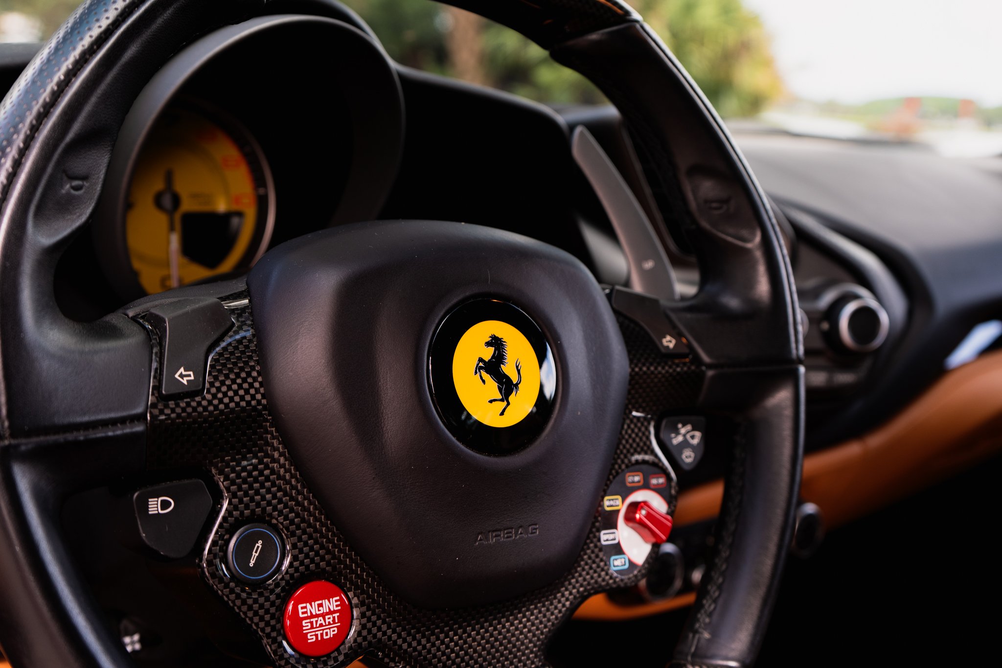 Close-up of a Ferrari steering wheel with various controls and the Ferrari logo at the center, inside a car on a highway.
