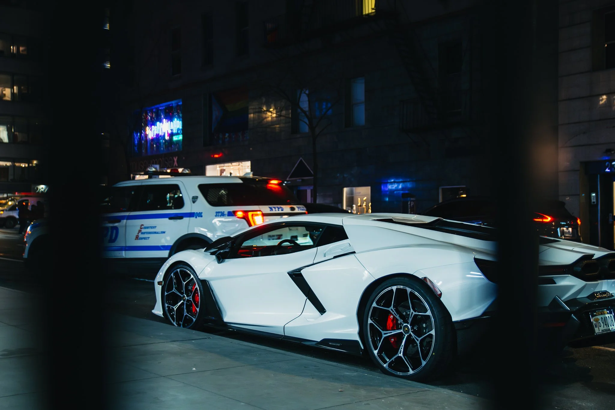 A white Lamborghini sports car parked on city street at night, with police vehicles nearby.