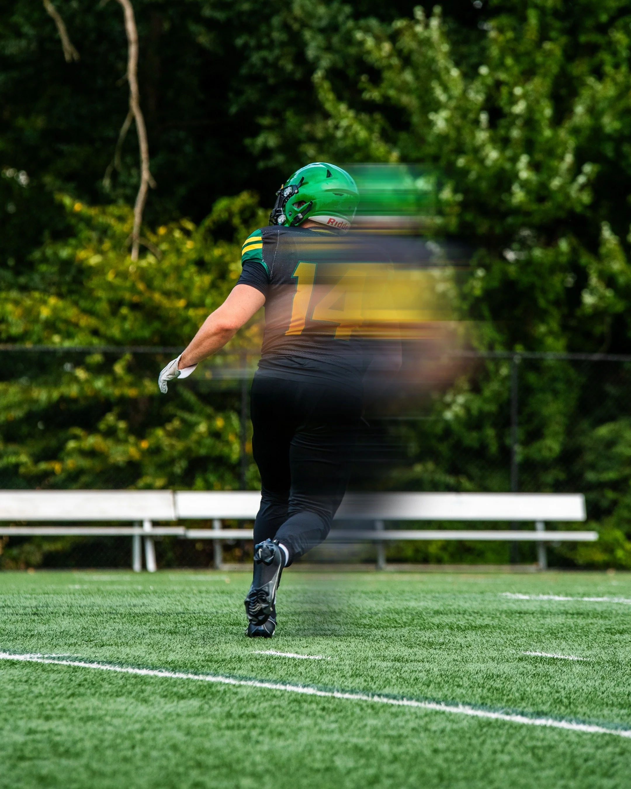 A football player in a black uniform with green, yellow, and white accents, wearing a green helmet, is running on a field with motion blur.