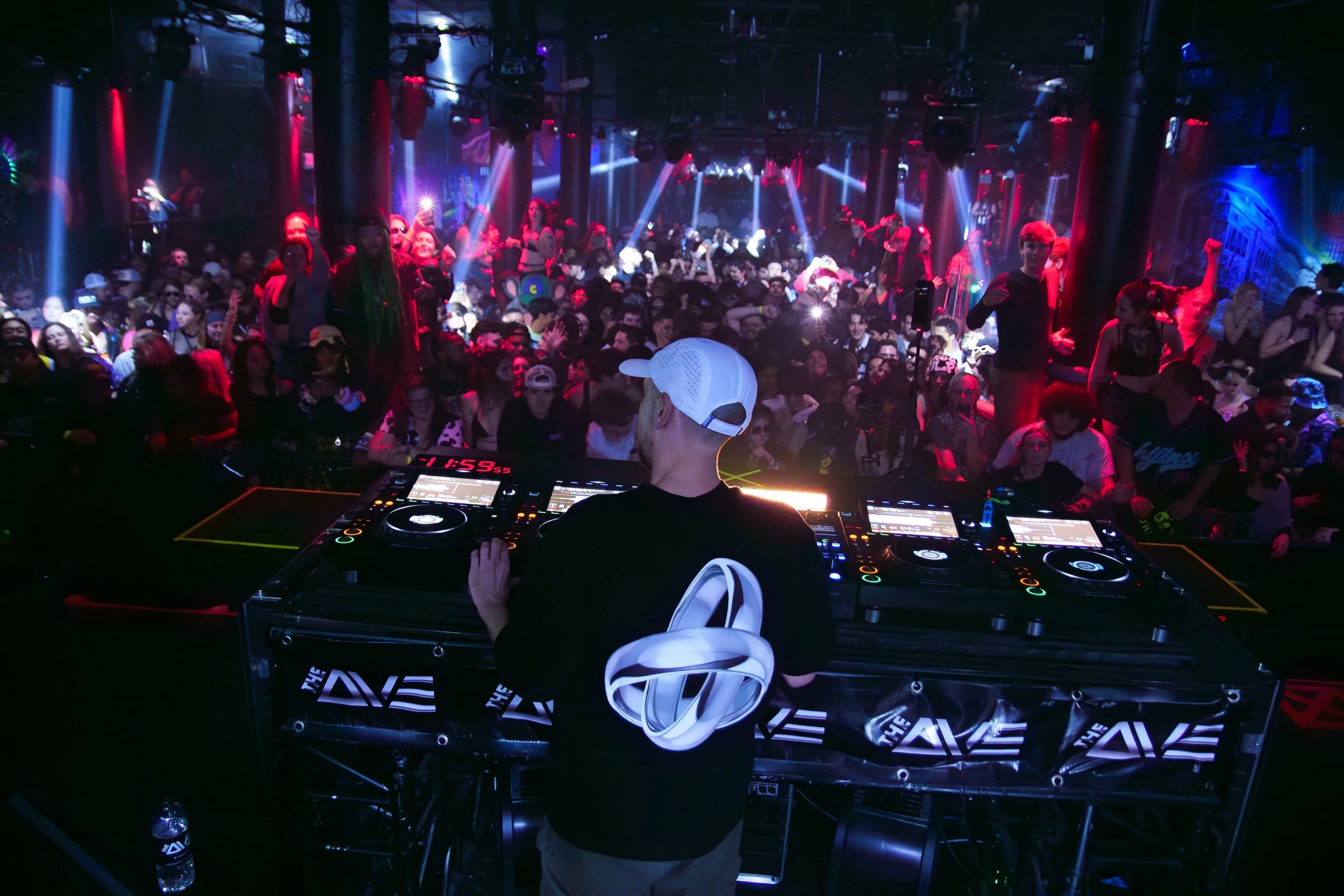 DJ performing at a nightclub with a crowd dancing and enjoying the music under colorful lights.