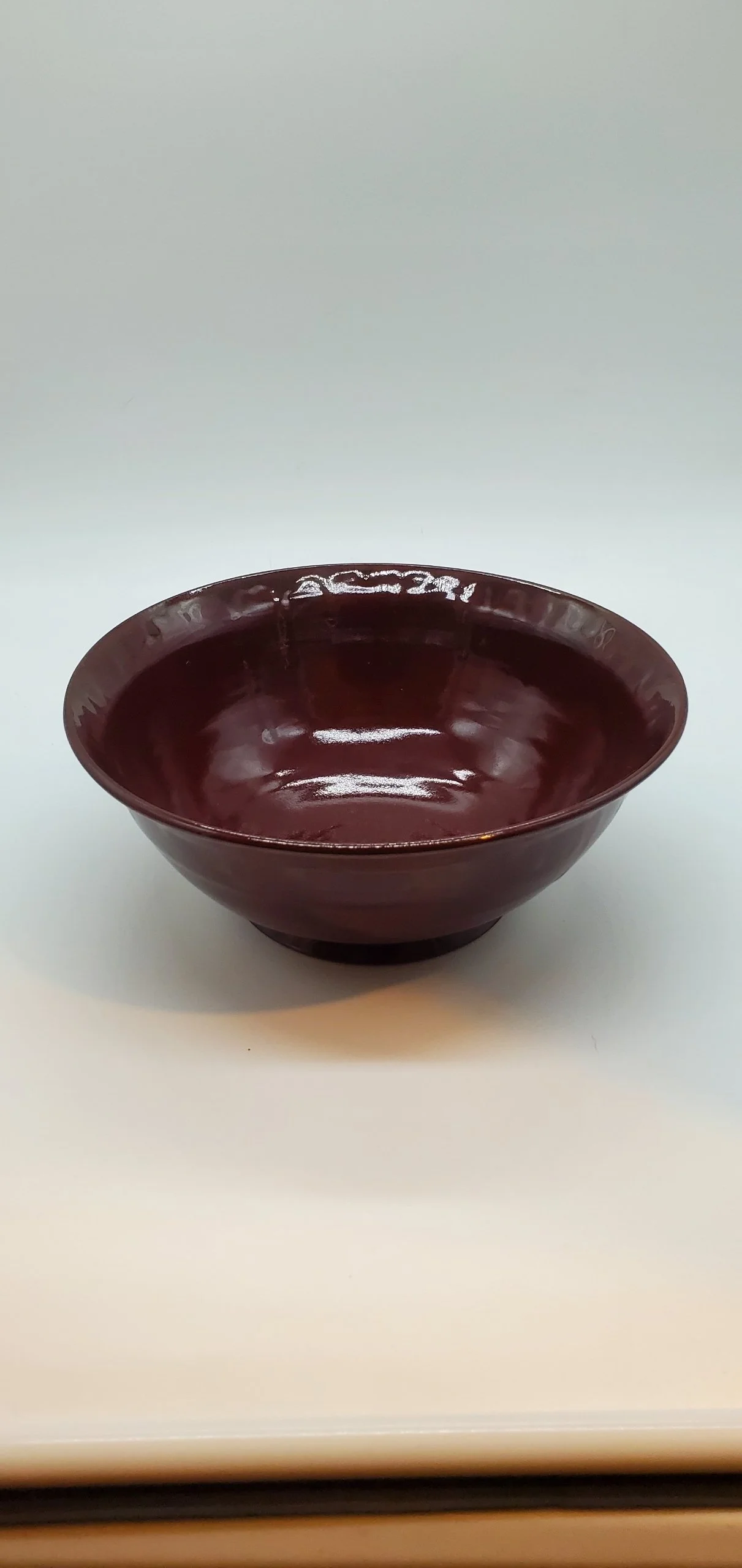 A dark red ceramic bowl with a shiny finish on a white surface with a plain white background.