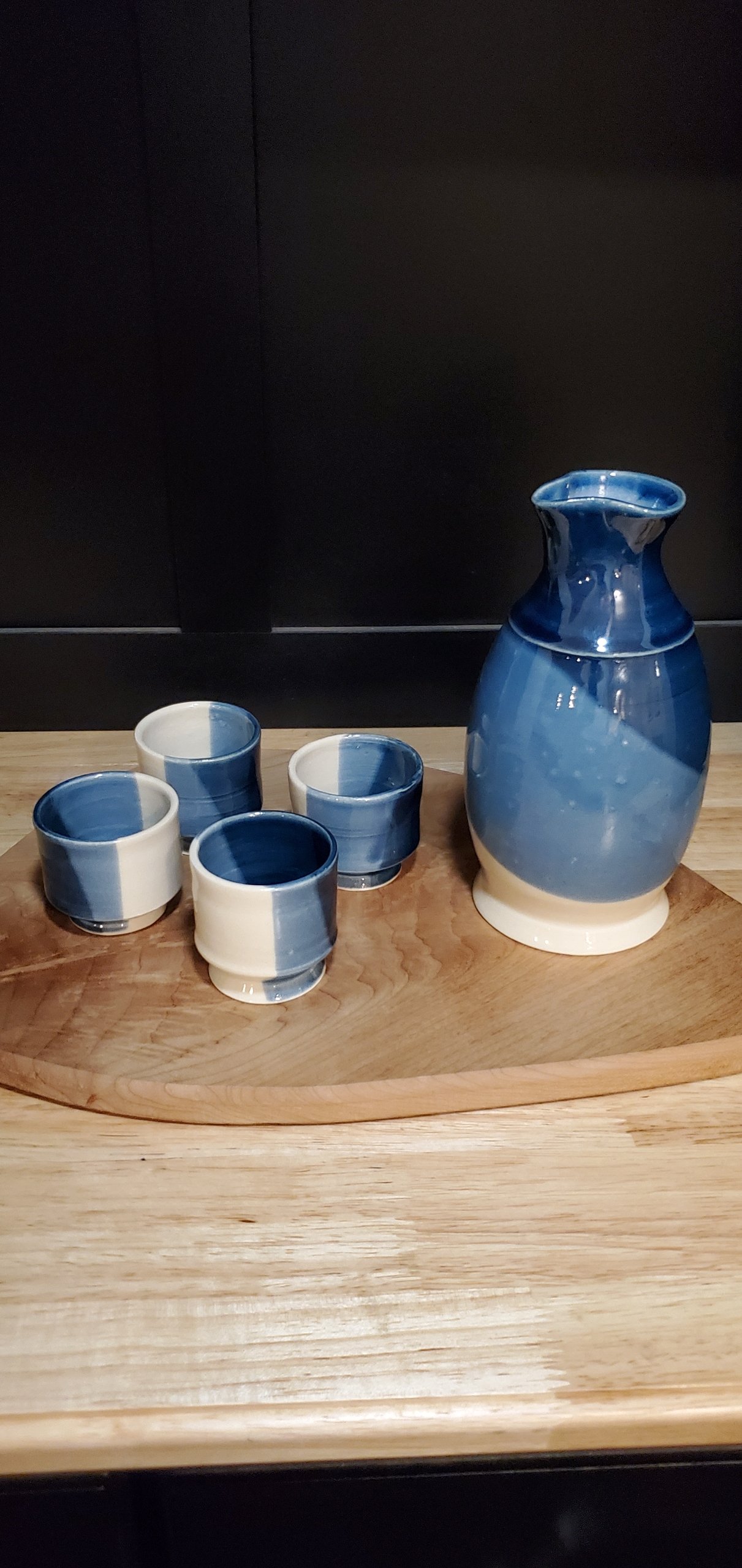 A ceramic blue and white pitcher and four matching cups on a wooden tray.