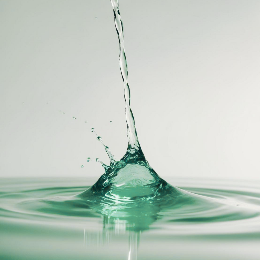 Close-up of water splash with a vertical stream of water falling into a calm water surface against a plain background.