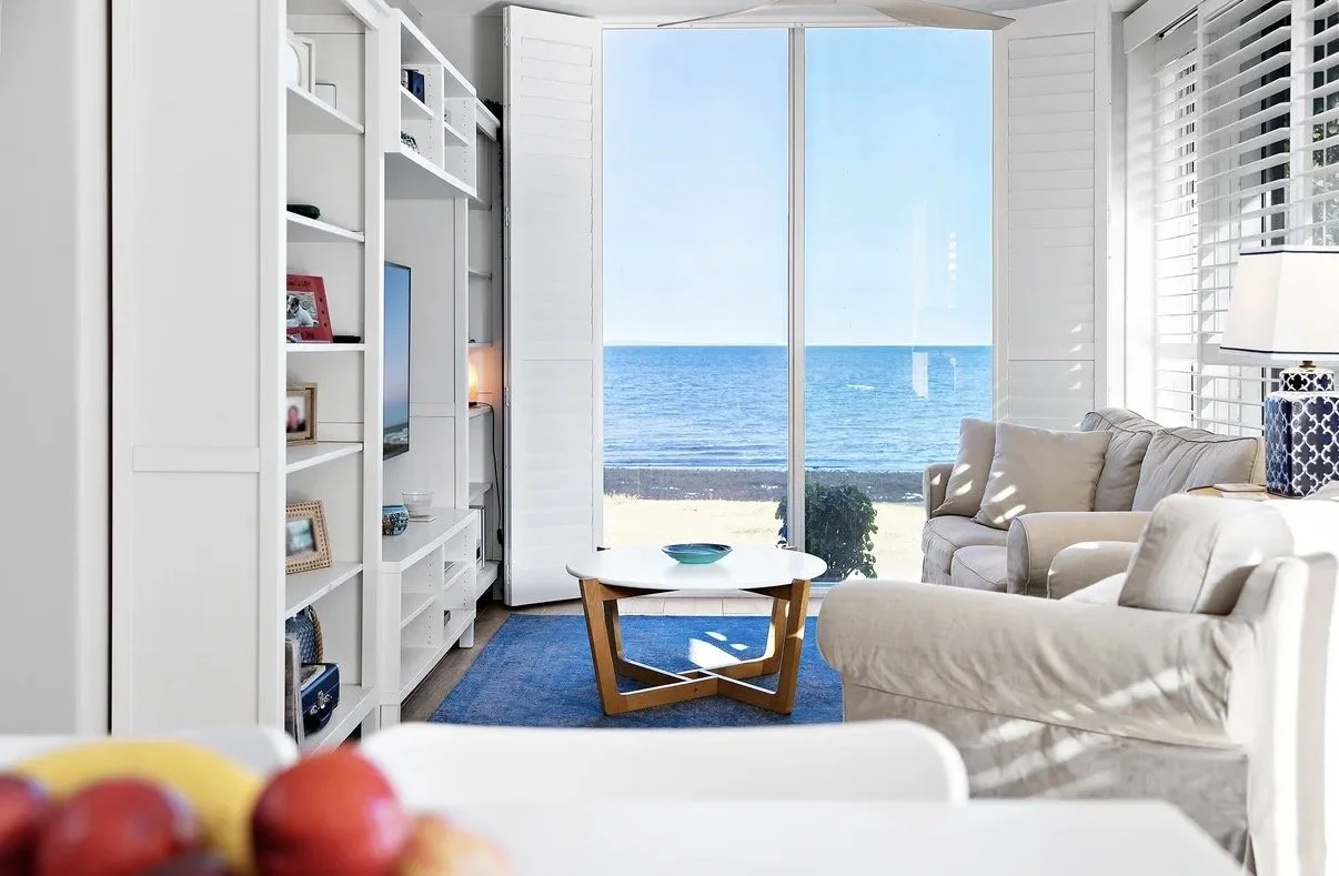 Bright coastal living room with large window, ocean views and neutral furnishings
