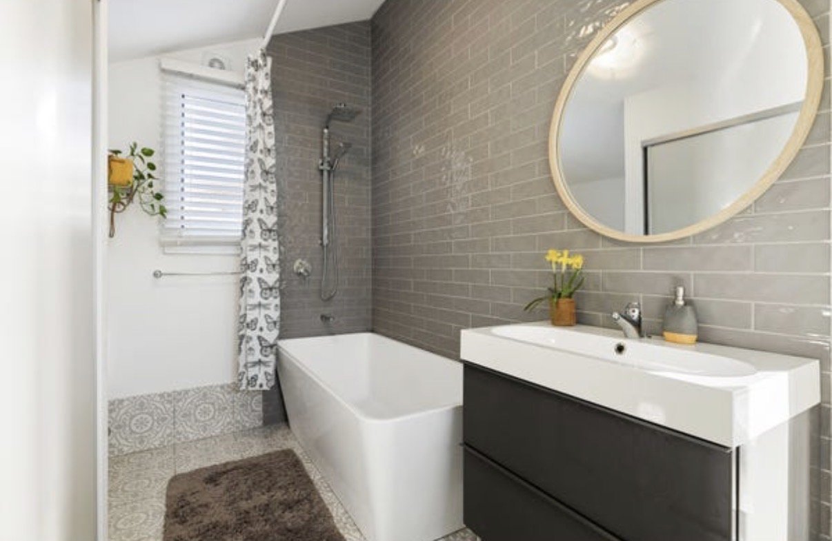 Modern bathroom with freestanding bath, grey tiles, round mirror and timber vanity