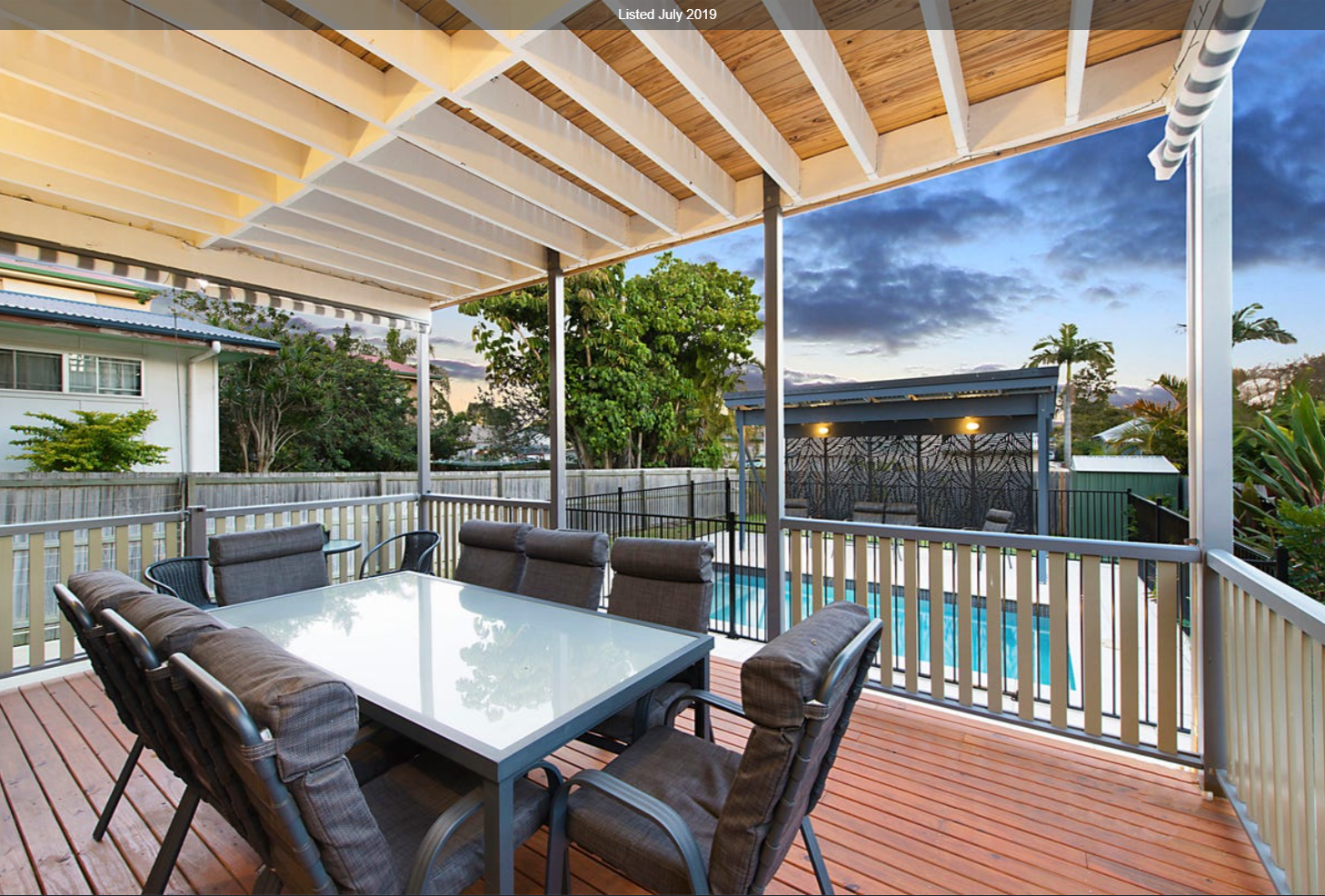 Covered outdoor deck with dining setting overlooking pool and backyard