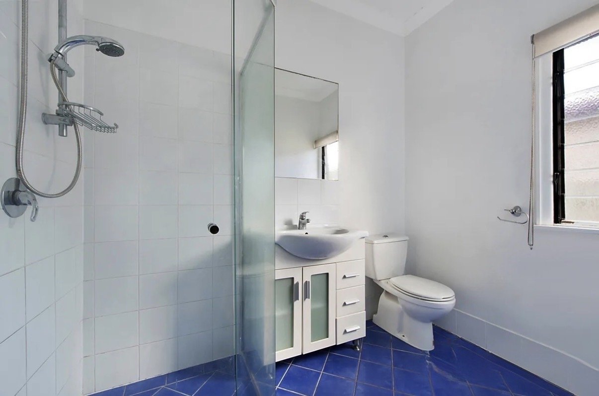 Original bathroom with blue floor tiles, glass shower and small vanity