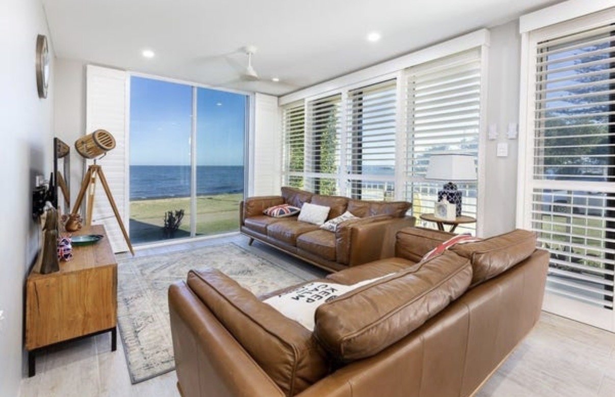 Modern living room with leather sofas, large windows and coastal outlook