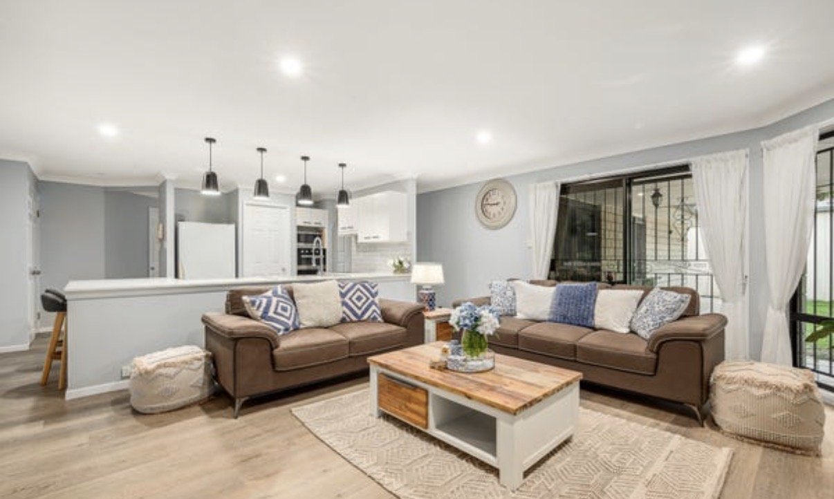 Open-plan living area with leather sofas, timber coffee table and white kitchen with pendant lighting