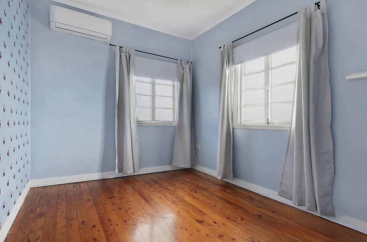 Empty bedroom with timber floors, wall-mounted air conditioner and two windows