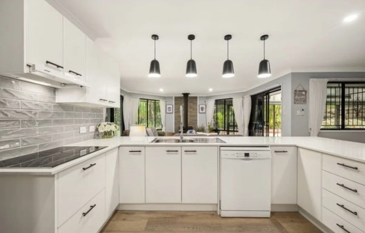 White U-shaped kitchen with stone benchtops, tiled splashback and black pendant lights