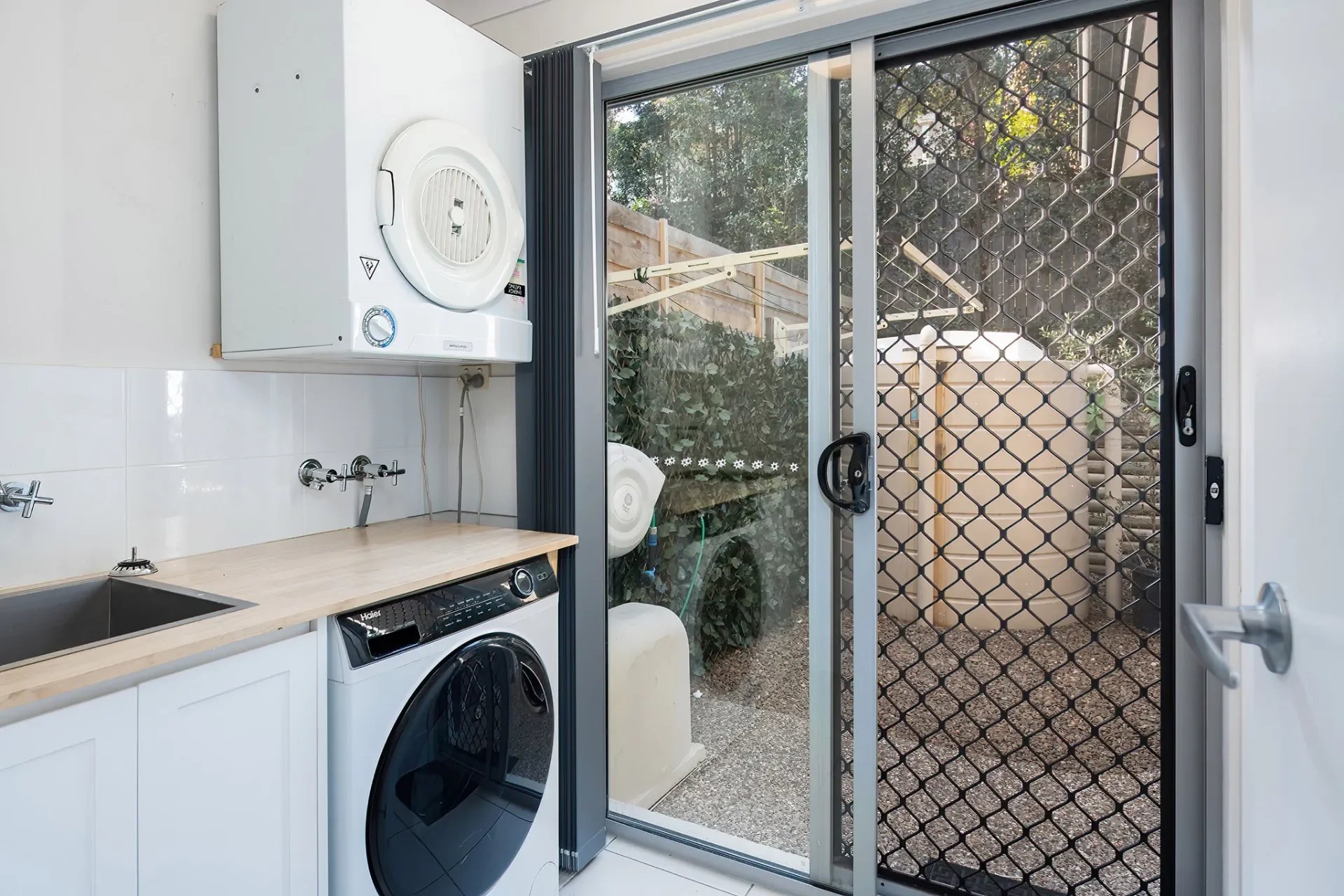 Compact laundry with cabinetry, washing machine and outdoor access via sliding door