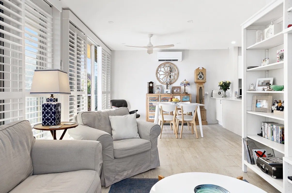 Open-plan living and dining area with light tones, built-in shelving and air conditioning