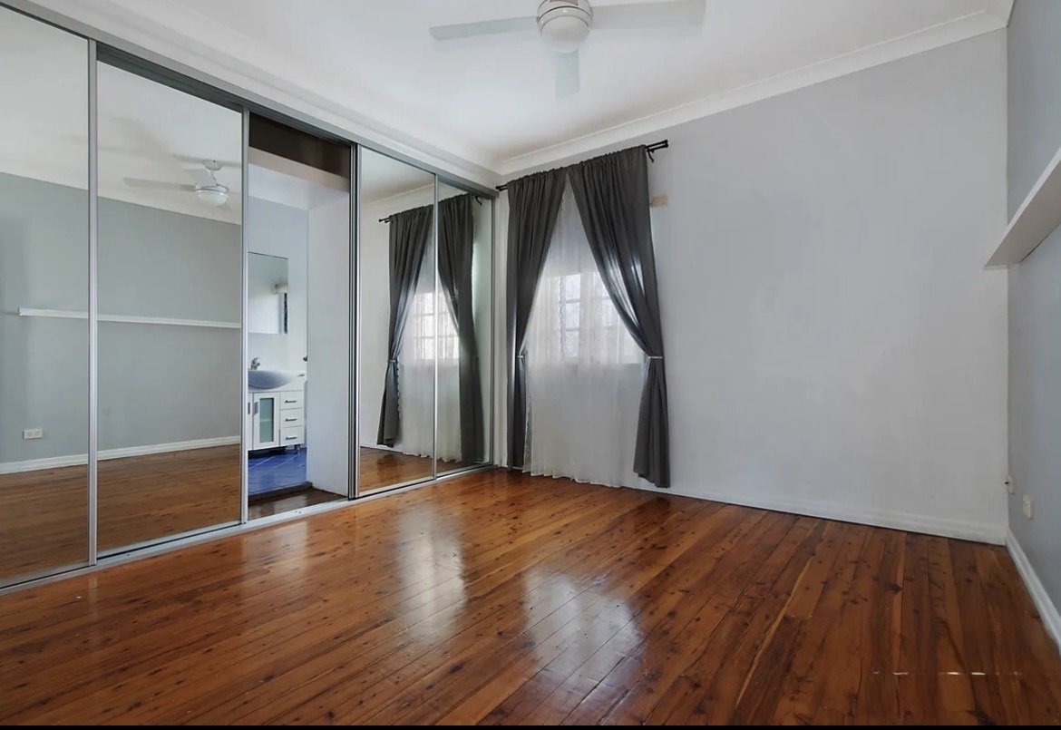 Bedroom with timber floors, mirrored built-in wardrobe and dark curtains