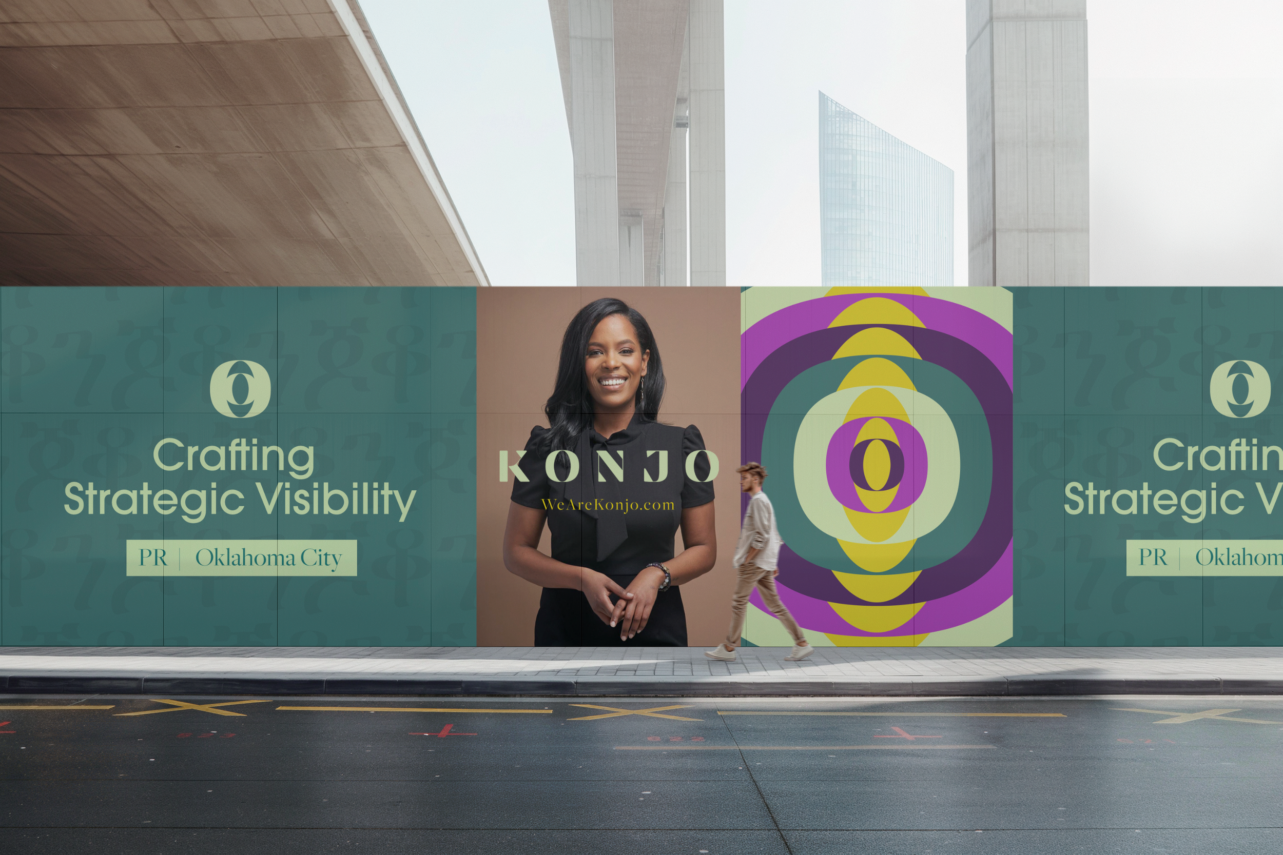 A large city street with a modern bridge overhead. A building with glass windows is visible in the background. A colorful billboard advertising branding services for Oklahoma City, featuring images of a woman smiling, a woman walking, and abstract colorful circles.