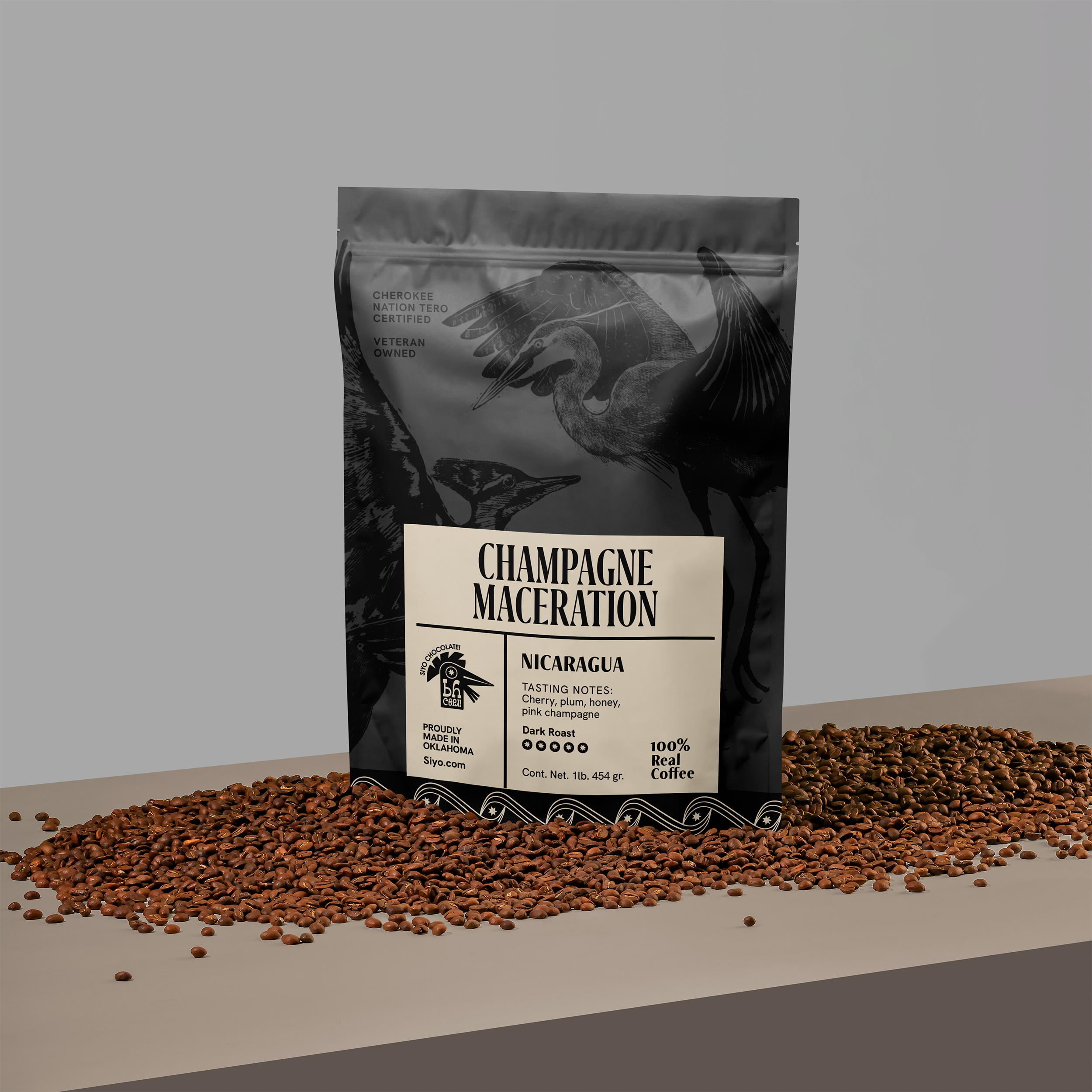 A black and white bag of coffee beans labeled 'Champagne Maceration' with Nicaragua origin information, tasting notes of cherry, plum, honey, pink champagne, on a beige surface, with scattered coffee beans in front.