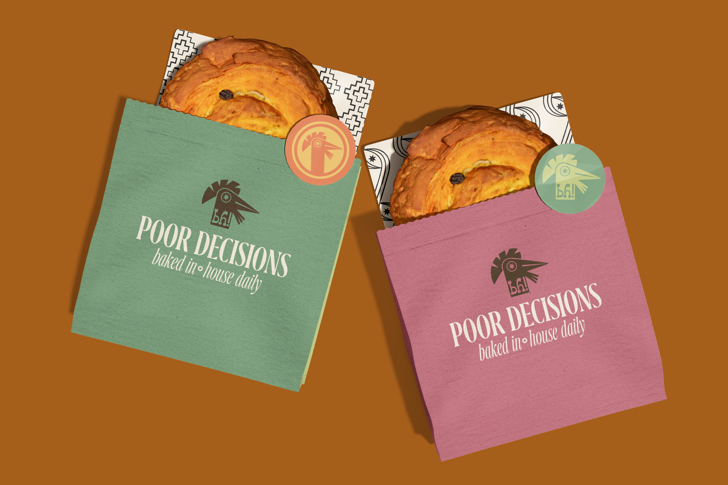 Two paper bags, one green and one pink, each containing a baked pastry with a raisin on top. The bags have a logo of a stylized rooster and the phrase "Poor Decisions baked in house daily." The green bag has a pink circular sticker, and the pink bag has a green circular sticker. The bags are placed on a brown surface.