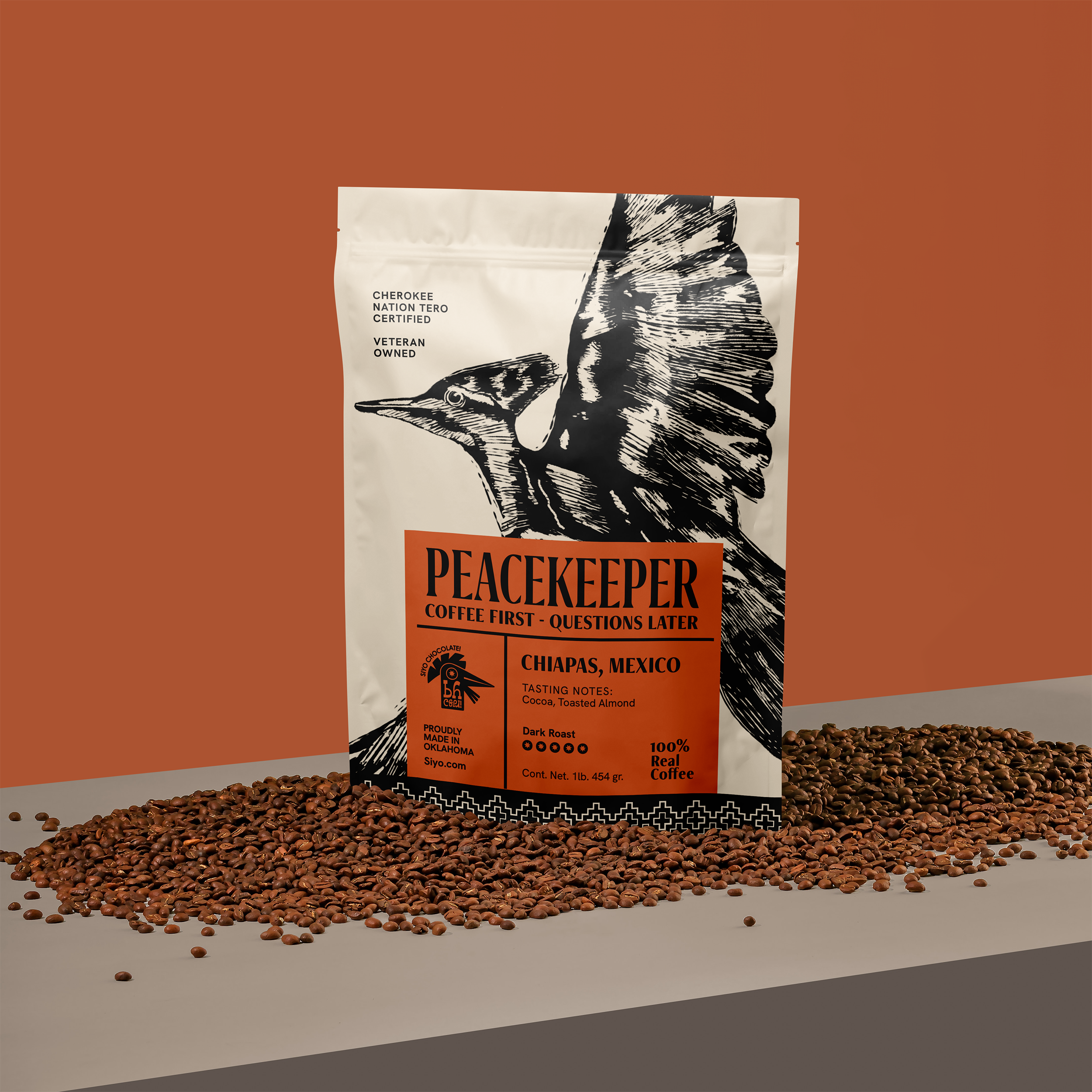 A bag of Siyo's Peacekeeper coffee with a hummingbird illustration on the label, surrounded by scattered coffee beans on a surface against an orange and beige background.