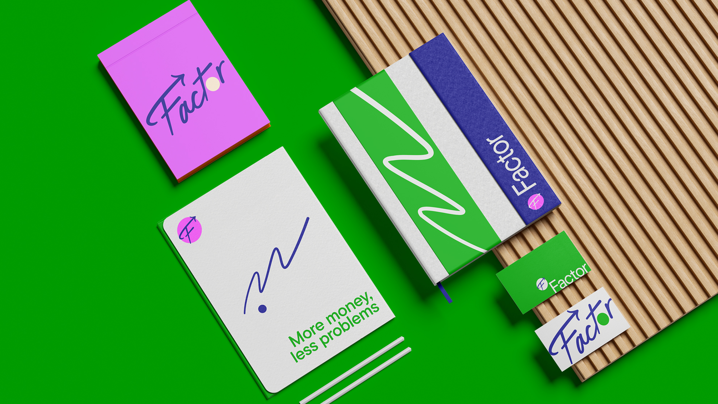 Collection of colorful stationery items including a white card with a question mark and green text "More money, less problems," a pink card with the word "Factor," a green and blue box labeled "Factor," a small green folder with a logo, and two white sticks, all arranged on a bright green background and wooden slatted surface.