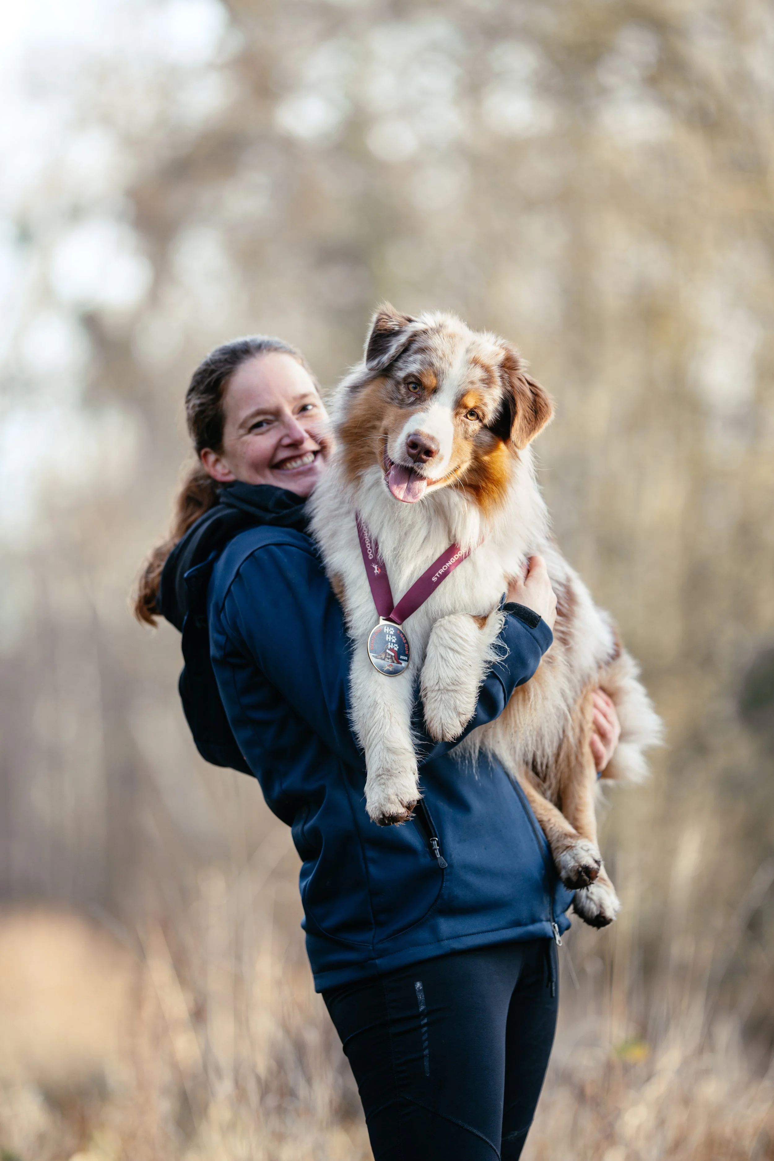 Frau hält einen Australian Shepherd Rüden mit einer StrongDog Medaille auf dem Arm.