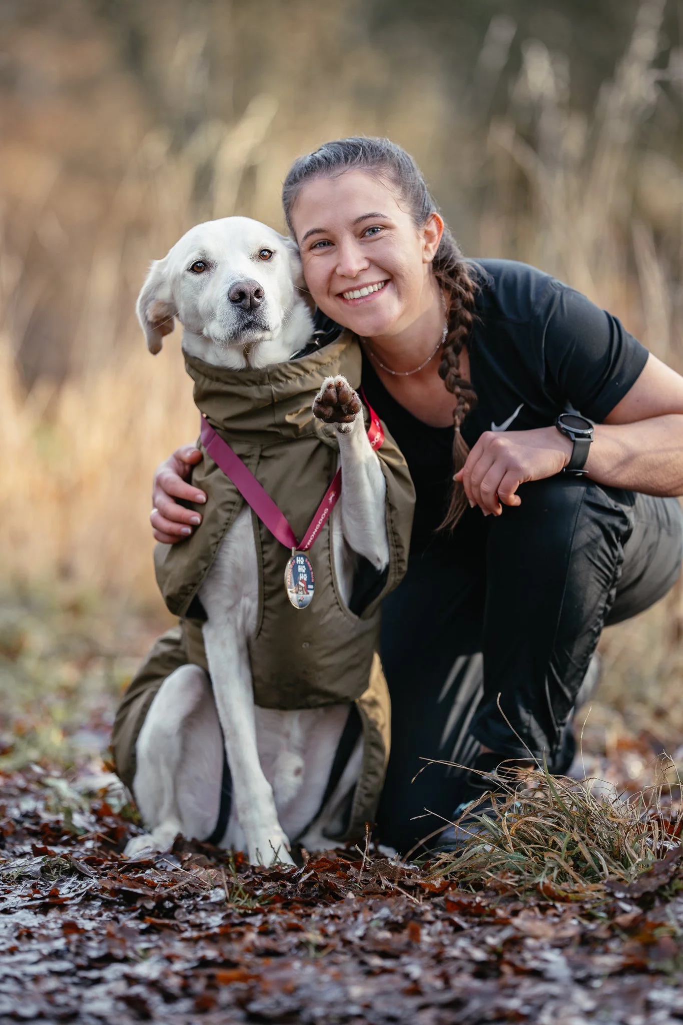 Frau und Hund im Freien in einer natürlichen Umgebung, sie lächelt, Hund trägt eine StrongDogMedaille.