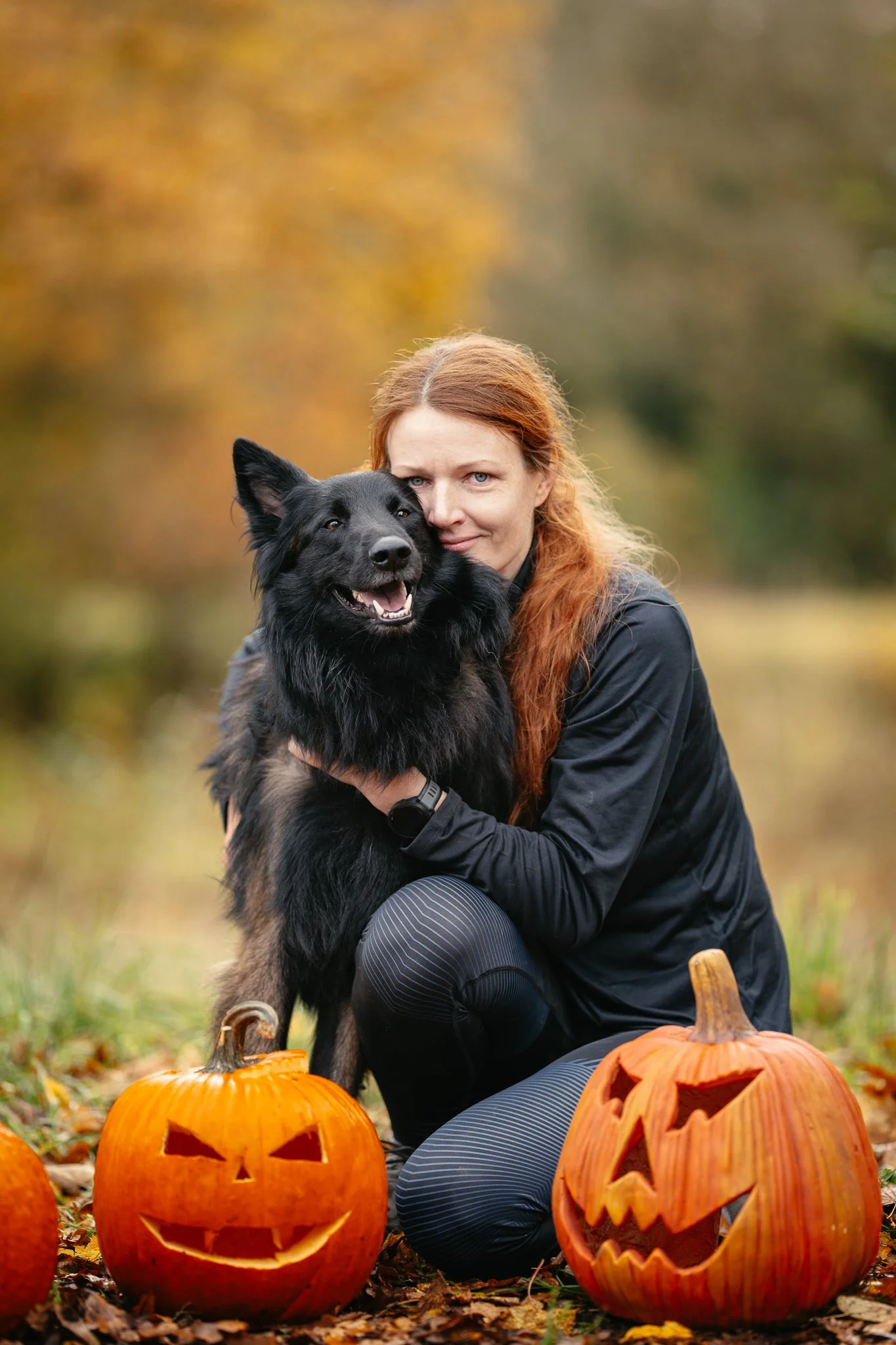 Eine Frau kniet im Freien und umarmt einen Schäferhund Tervueren sie lacht.