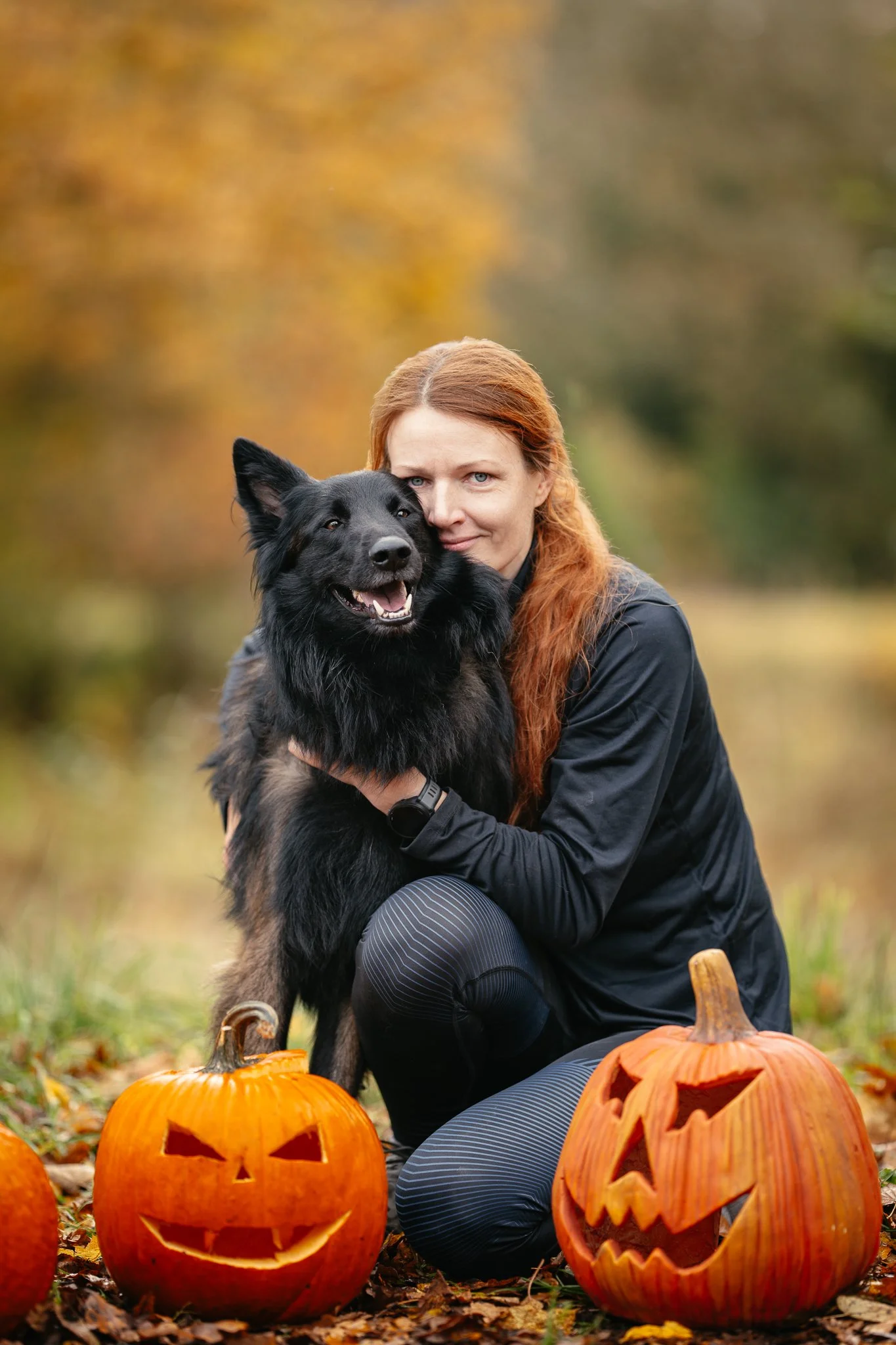 Eine Frau kniet im Freien und umarmt einen Schäferhund Tervueren sie lacht.
