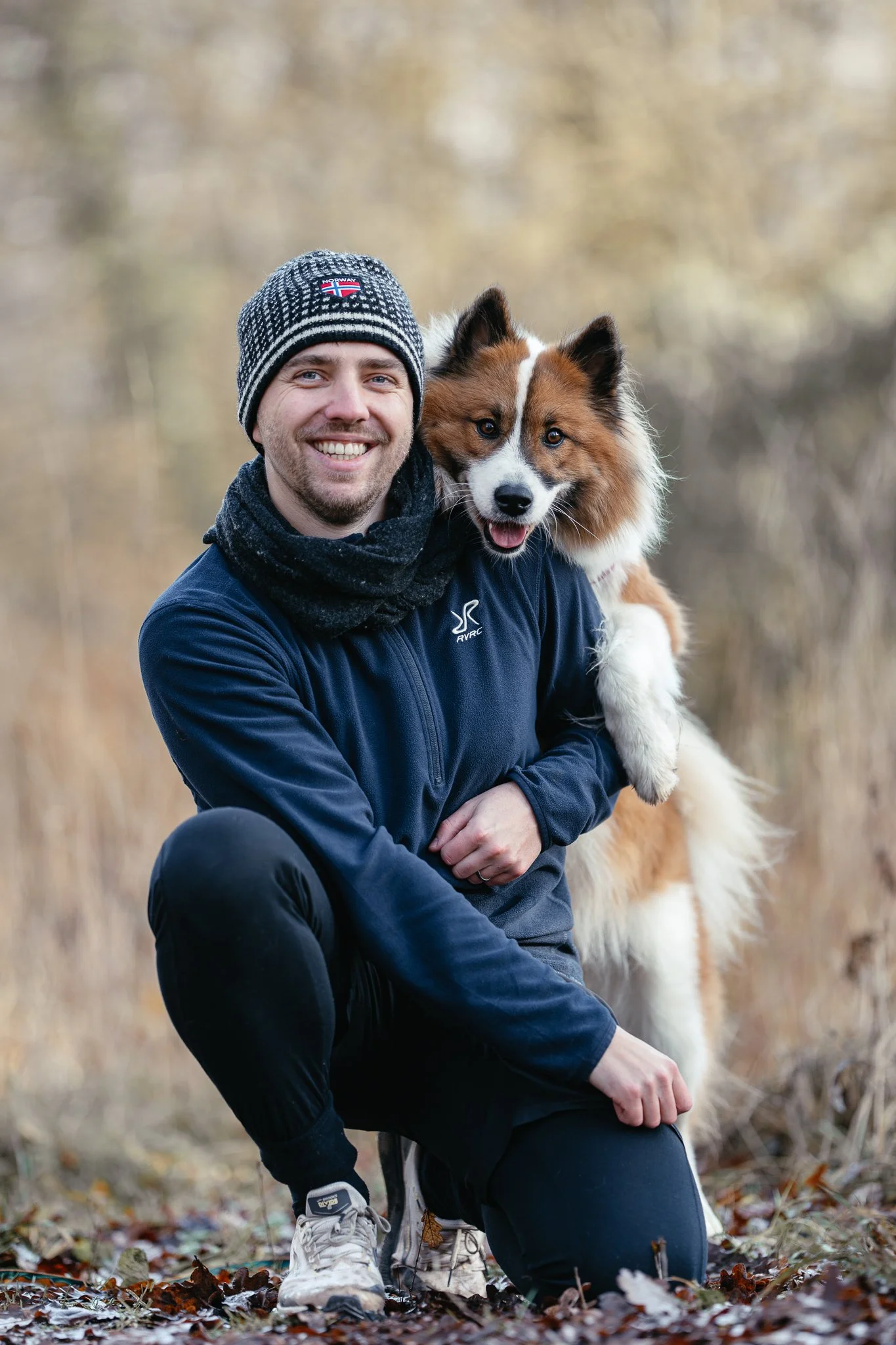 Ein Mann mit einer Elo Hündin im Freien, umgeben von Bäumen und Herbstlaub.
