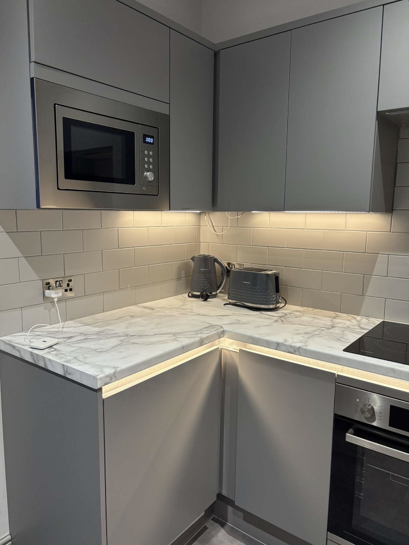 Modern kitchen corner with gray cabinets, marble countertop, built-in microwave, electric kettle, toaster, and stove.