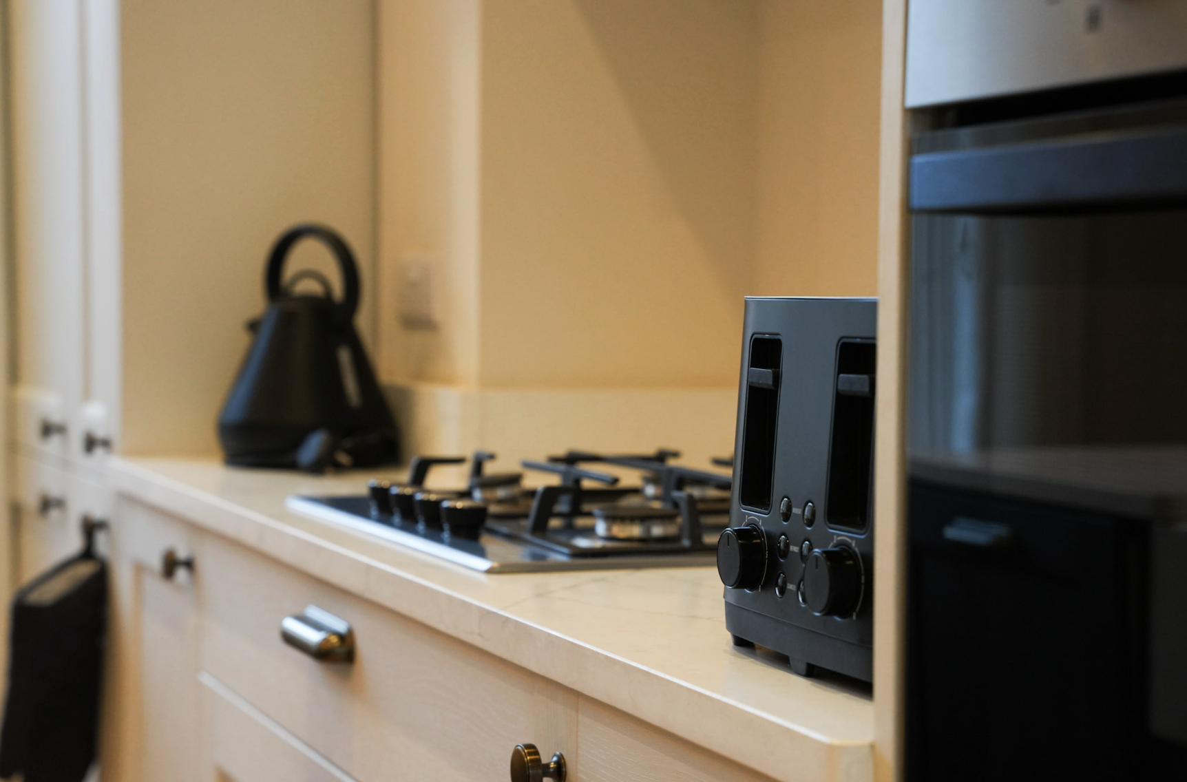 Kitchen countertop with a black toaster, a black electric kettle, and a gas stove with four burners. There are cabinets and drawers below the counter.