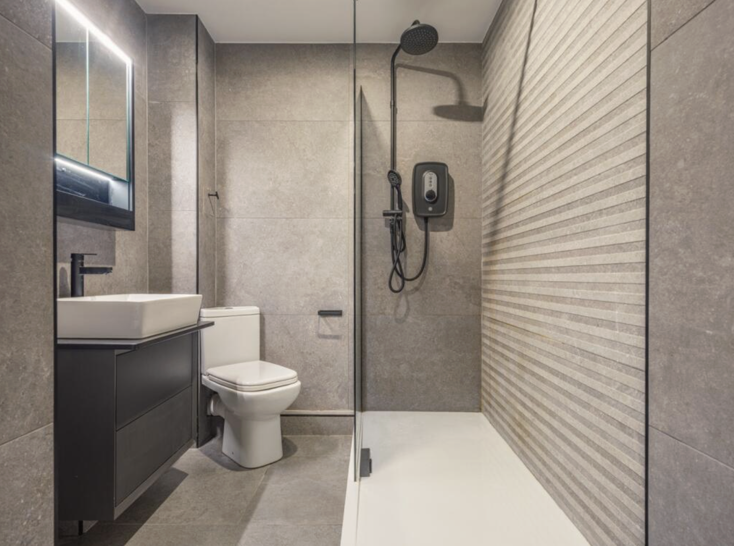 Modern bathroom with a walk-in shower, toilet, sink, and mirror with lights.