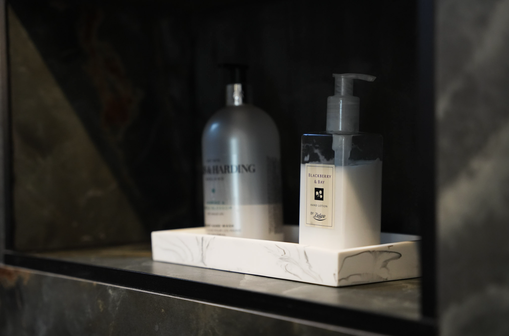Close-up of hand lotion and soap bottles on a white tray inside a dark shelf or cabinet.
