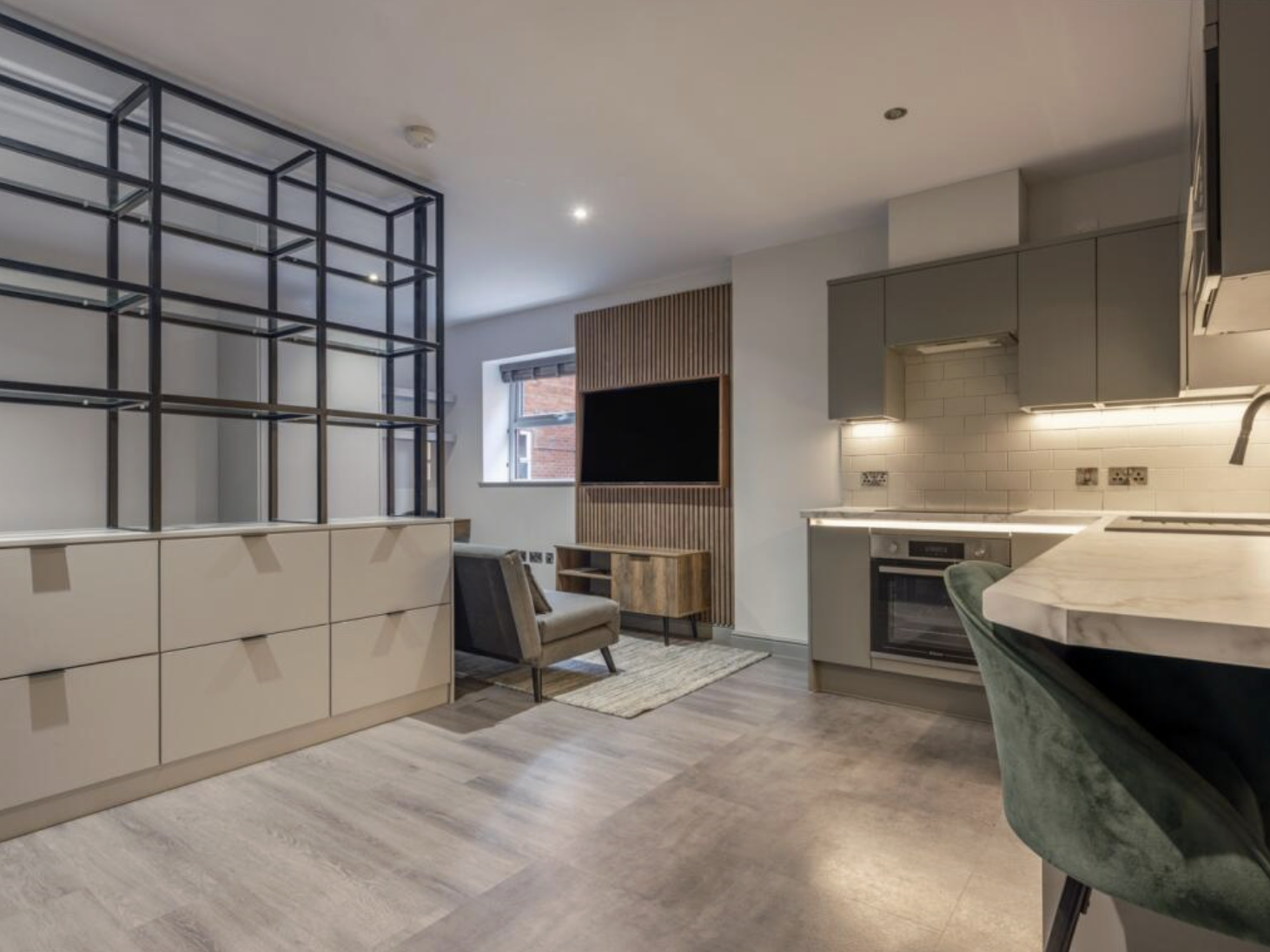 Modern open-concept living space with kitchen, seating area, and decorative shelving, featuring neutral tones, wood accents, and contemporary furniture.